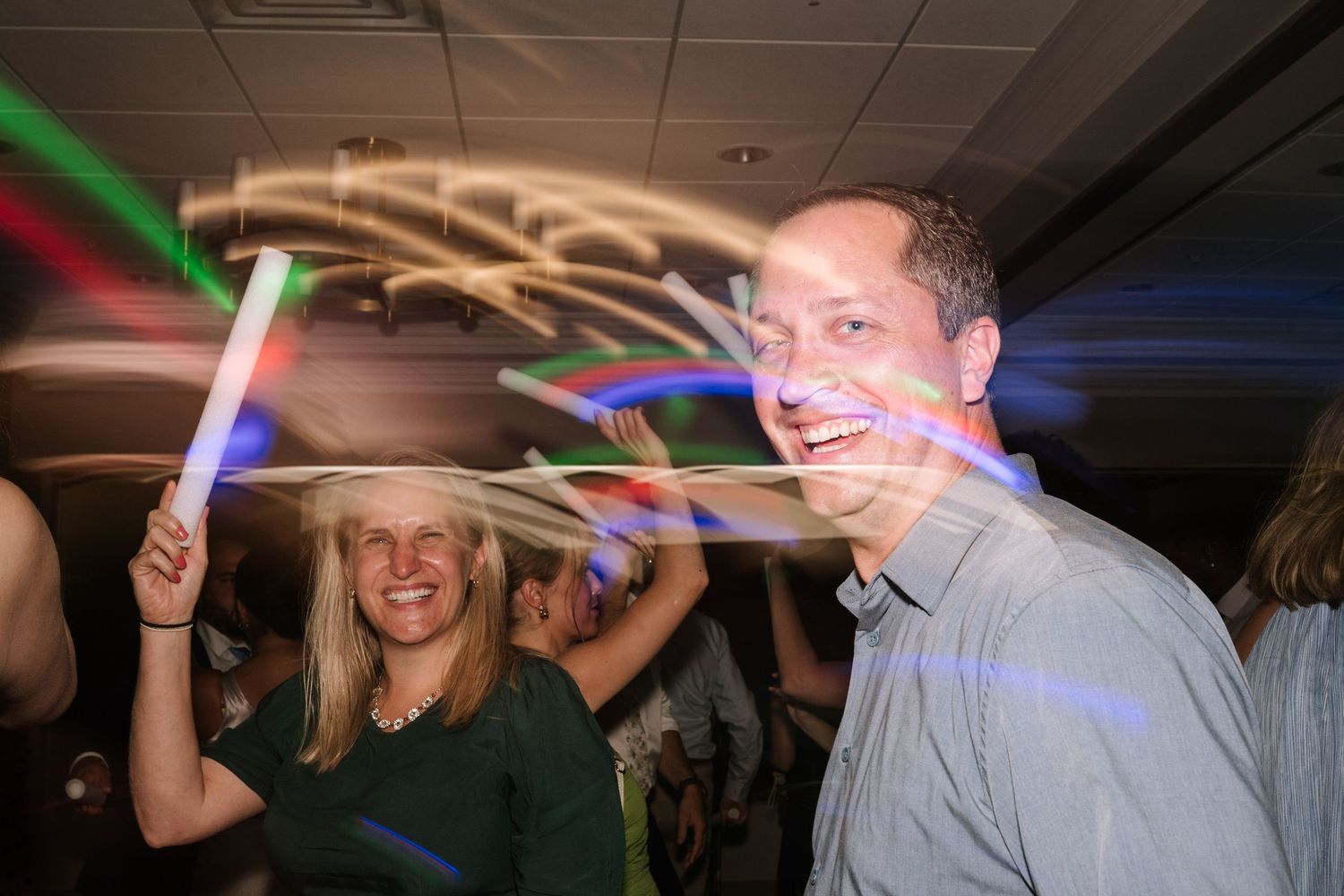 Wedding reception dance floor with colorful light trails and dancing guests.