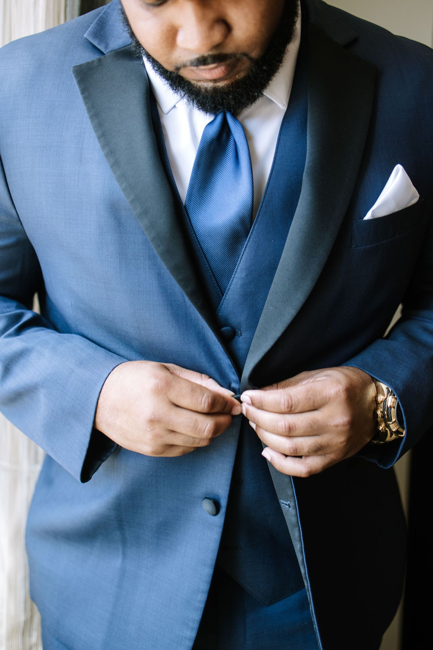 Close-up shots of a groom in a navy blue suit adjusting his tie and boutonniere before the wedding ceremony.