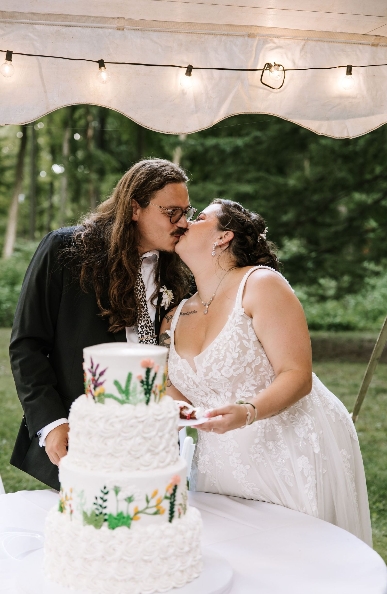 A couple sharing a moment while cutting their white wedding cake under string lights.