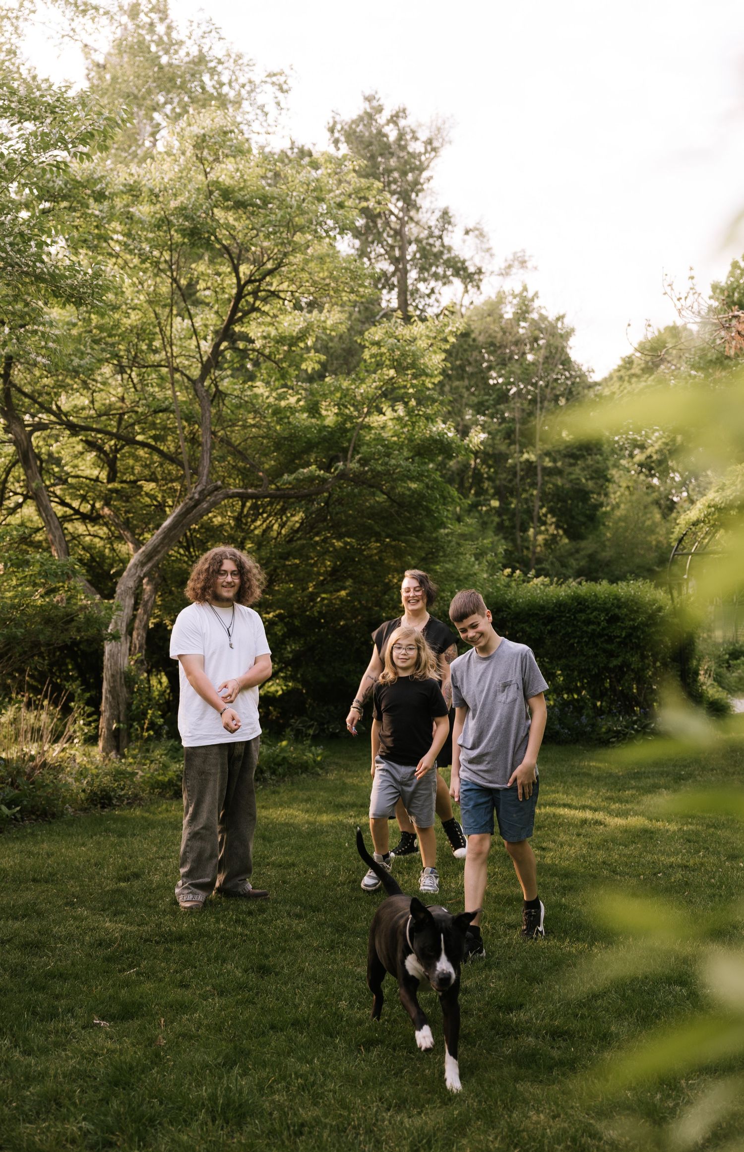 Family with dog playing in lush green backyard on sunny day.