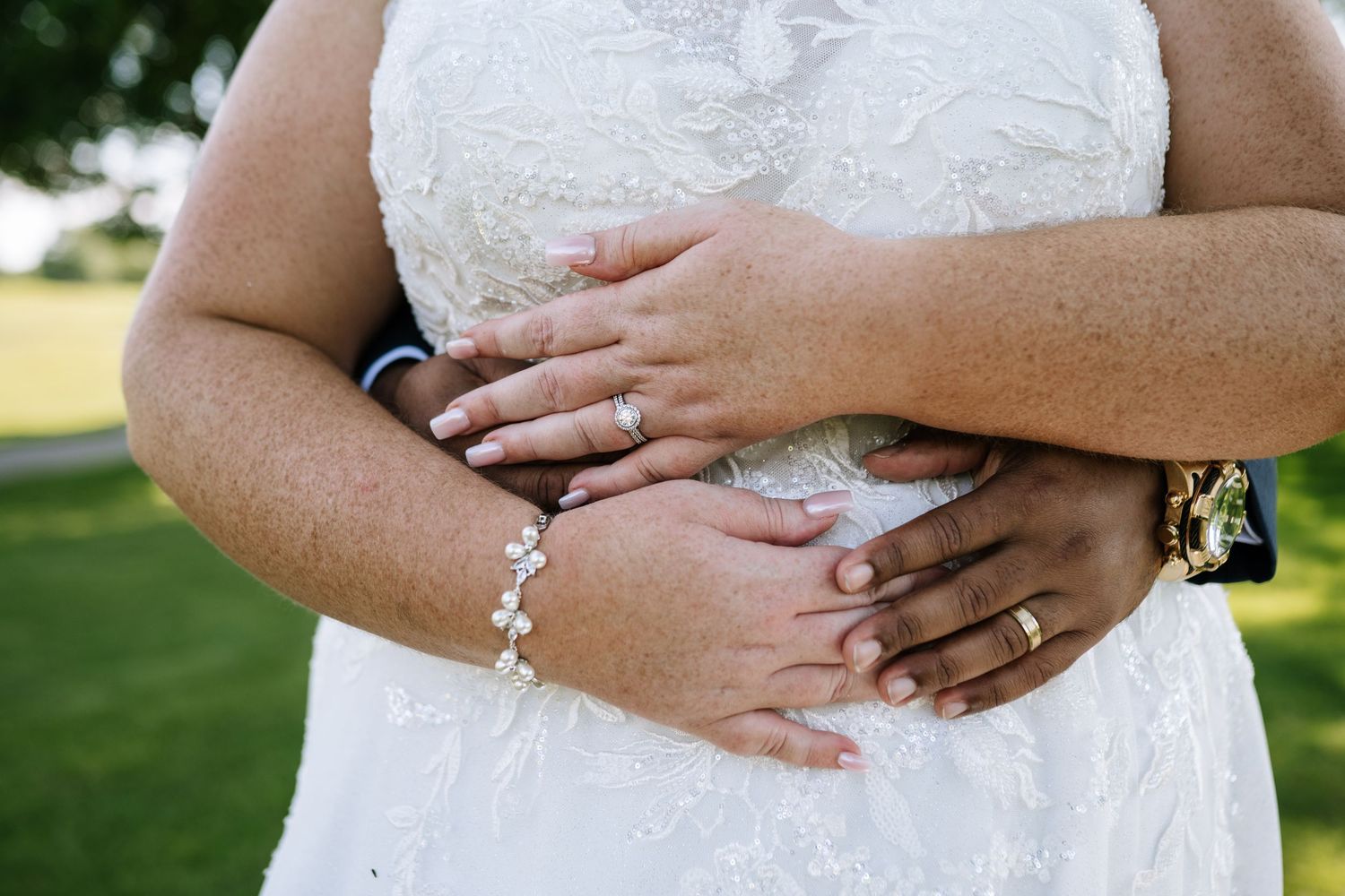 Close-up detail of couple's hands embracing showing wedding rings and lace dress.