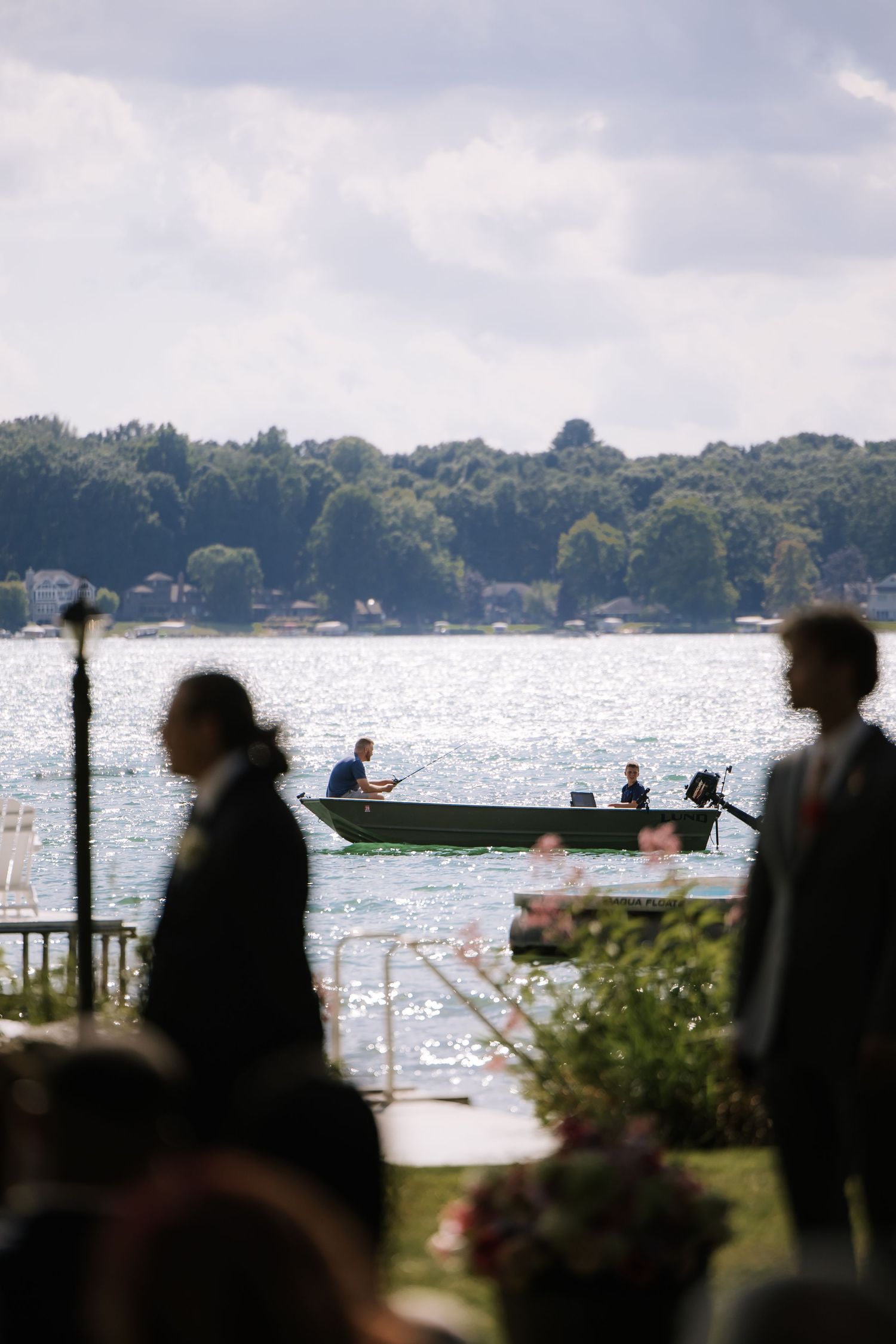 Silhouettes of guests gathered by a lakeside dock during a waterfront celebration.