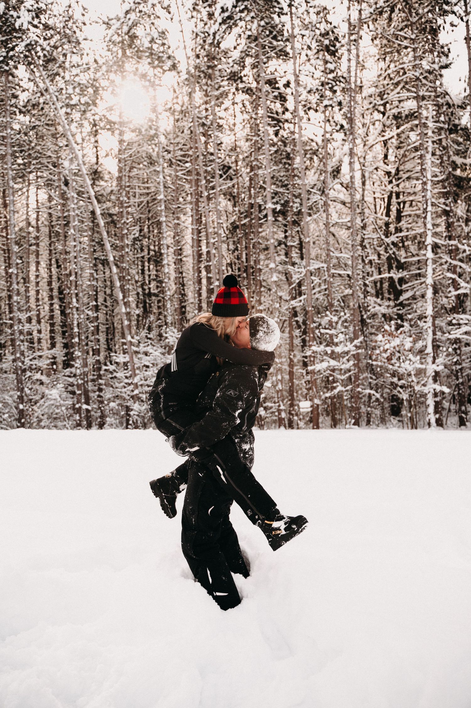A person in winter clothing jumps playfully in a snowy forest setting.
