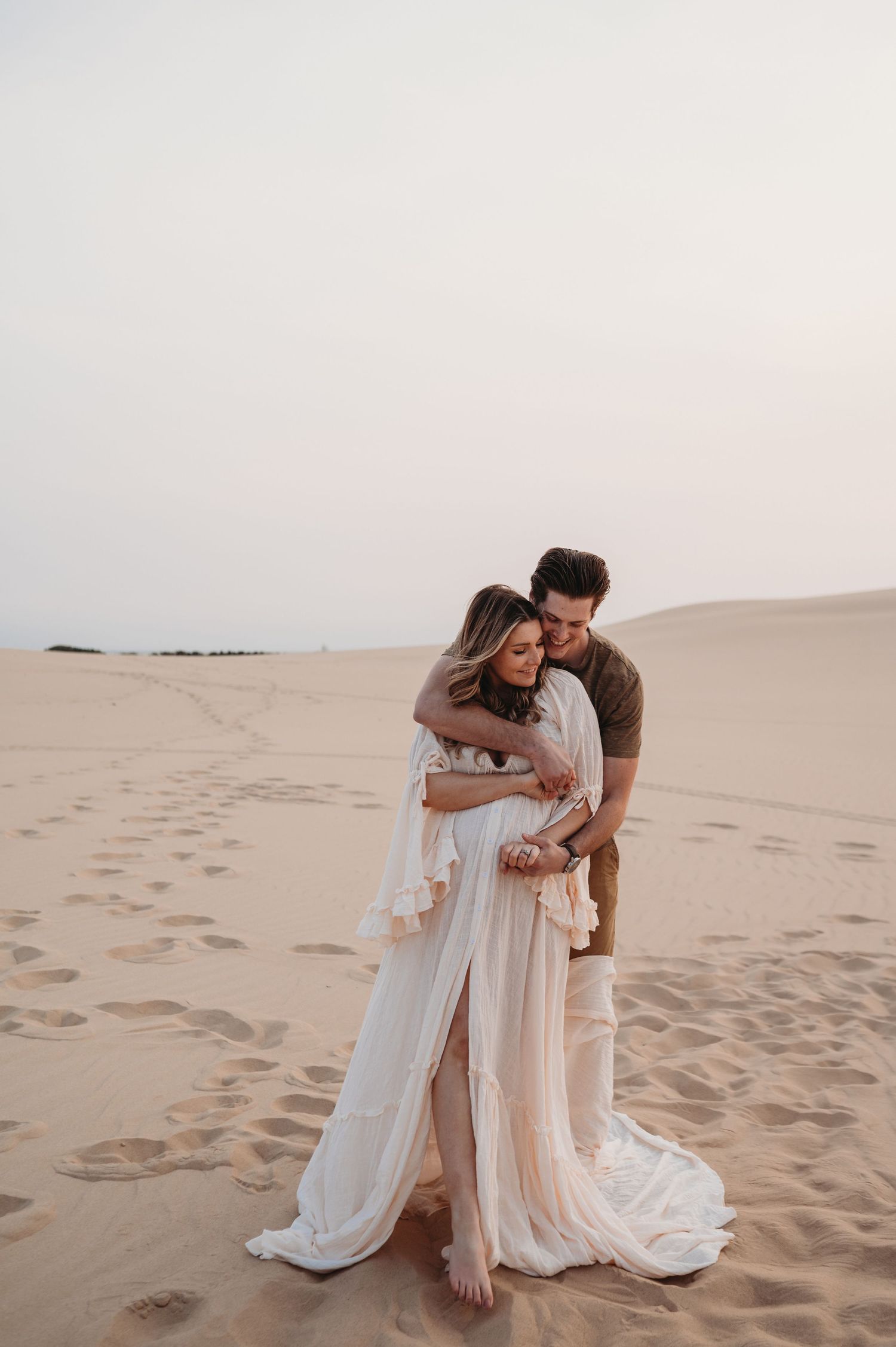 A couple shares an intimate moment on sandy dunes during a desert photoshoot.