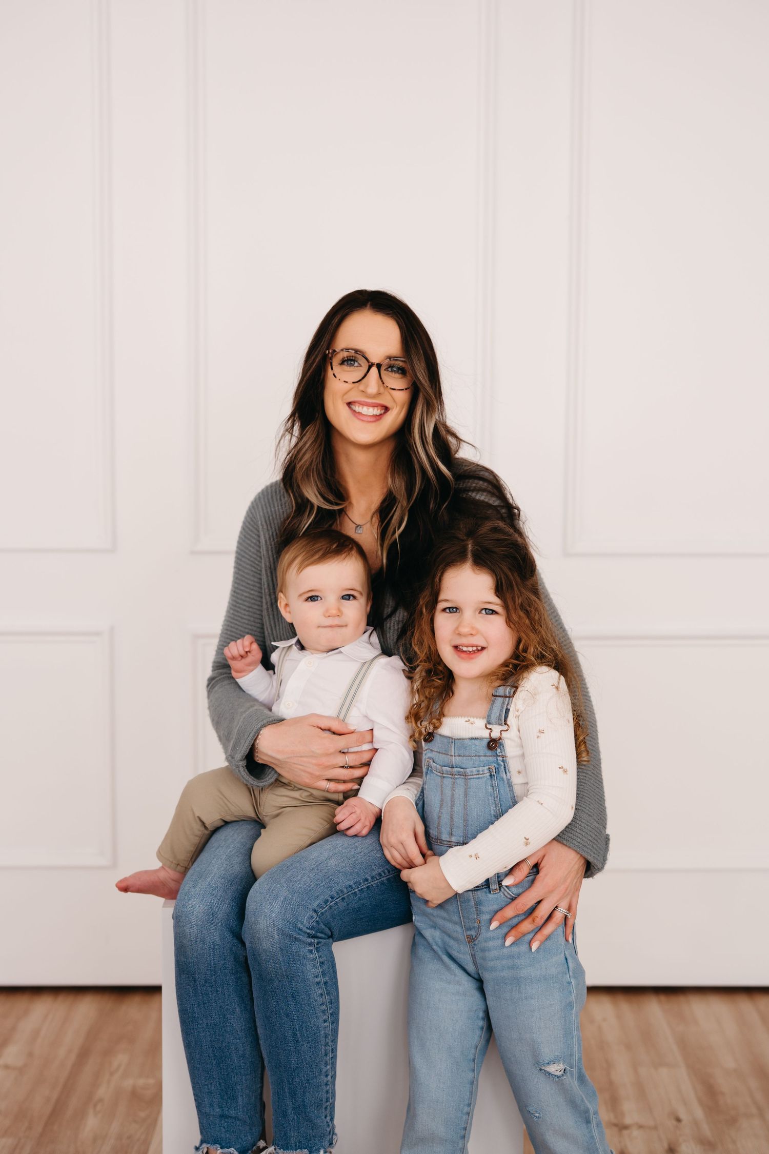 A family portrait against a white wall with children in casual attire on a hardwood floor.