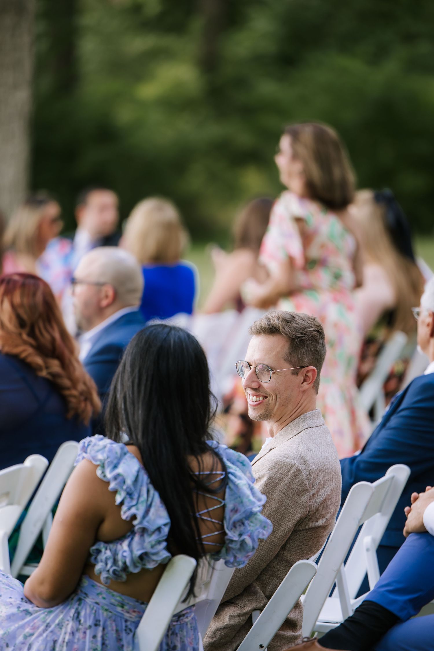 Wedding guests seated in white chairs during an outdoor ceremony.