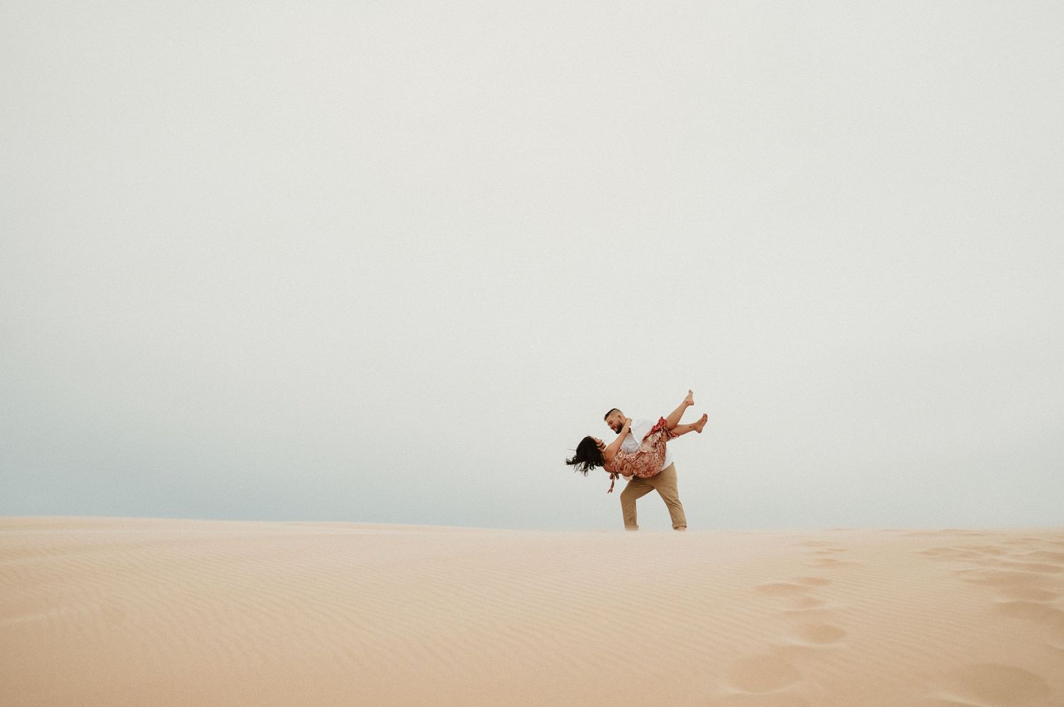 A playful couple dances and spins on top of a desert sand dune.