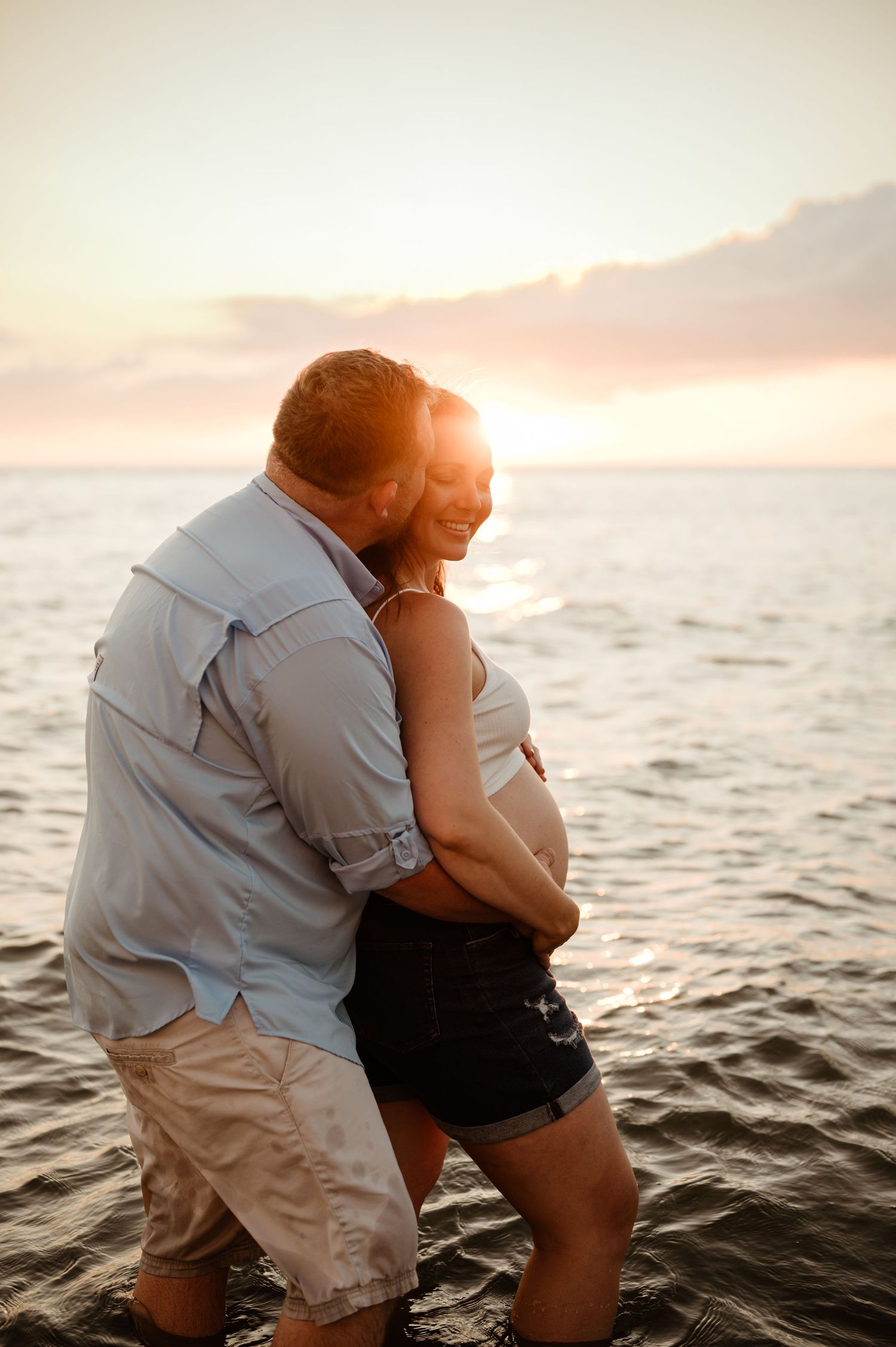 A couple embraces while standing in the ocean at sunset, creating a romantic silhouette against the warm sky.