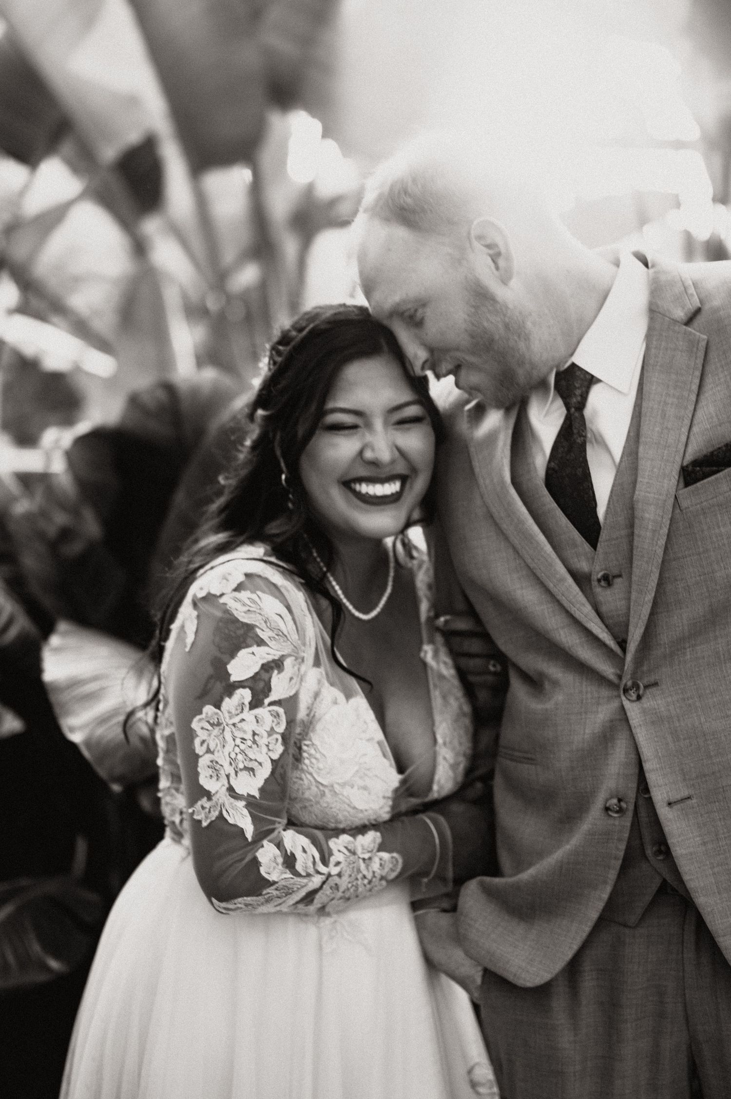 Black and white intimate wedding portrait surrounded by tropical foliage.