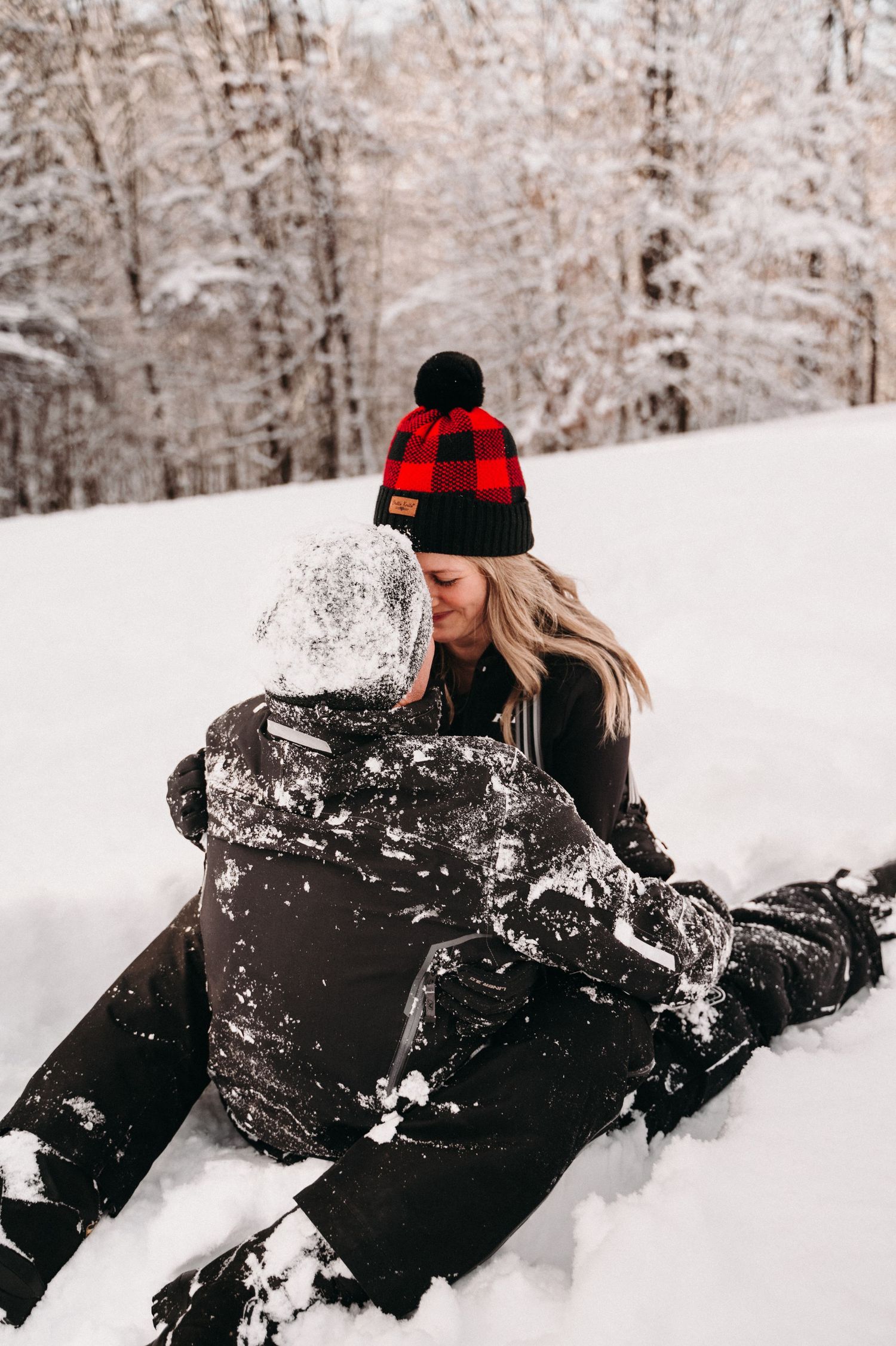 Couple in winter clothing sharing tender moment in snowy landscape.