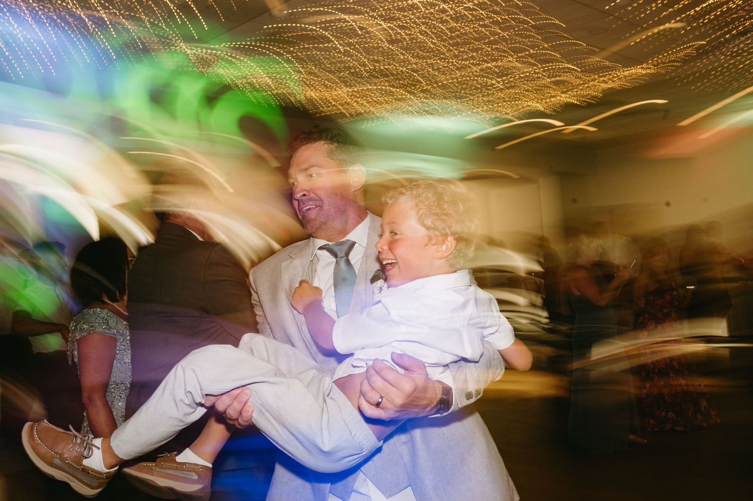 Motion-blurred photo of dancers celebrating at a wedding reception with colorful light effects.
