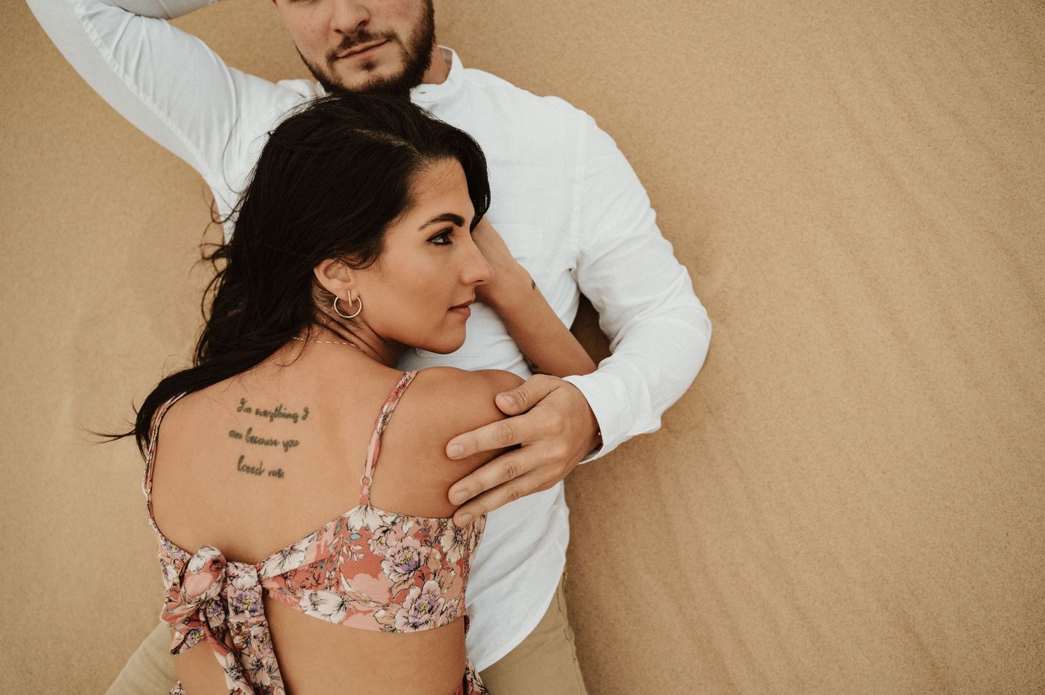 A couple poses intimately on sand dunes showing visible tattoo details.