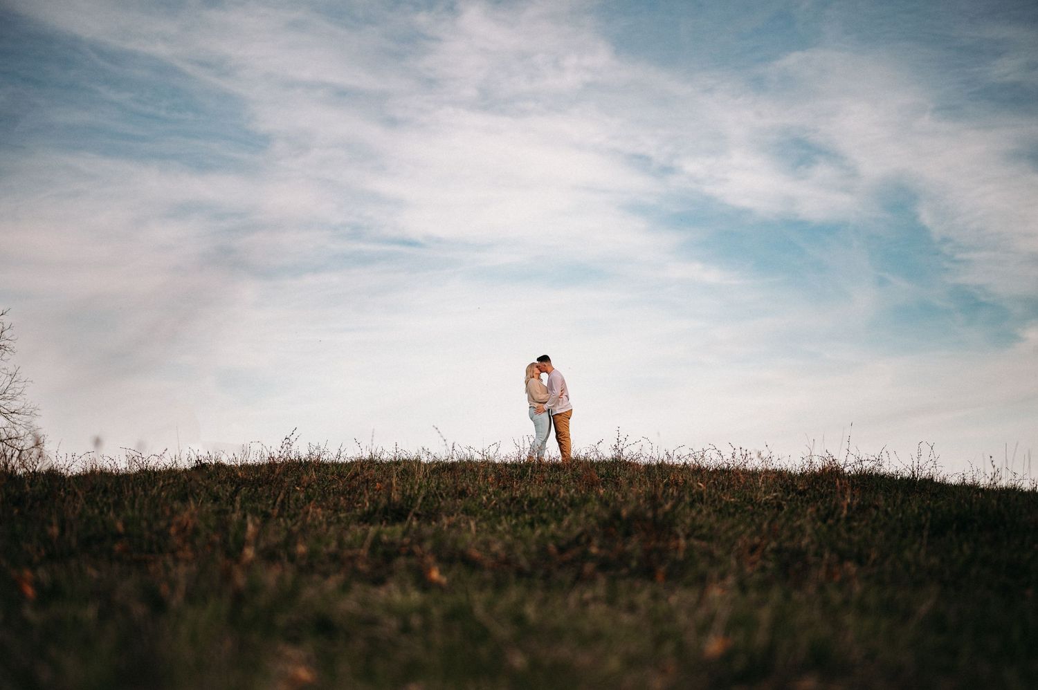 Silhouette of a couple standing on a hilltop against a cloudy blue sky.