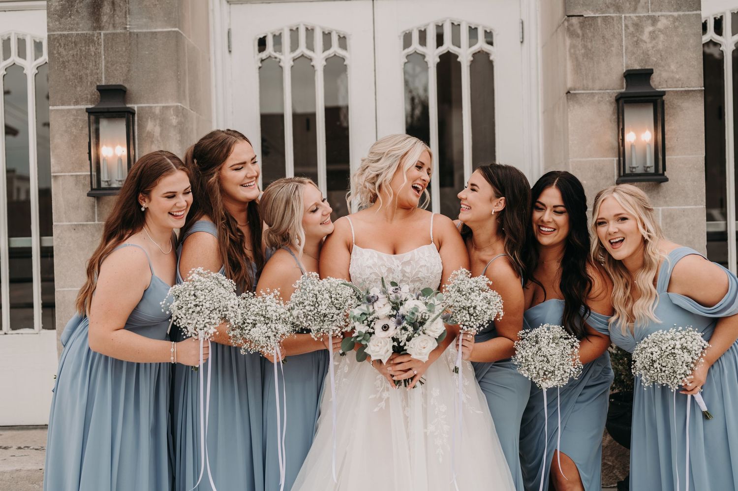 Wedding party in light blue dresses poses together with bouquets.