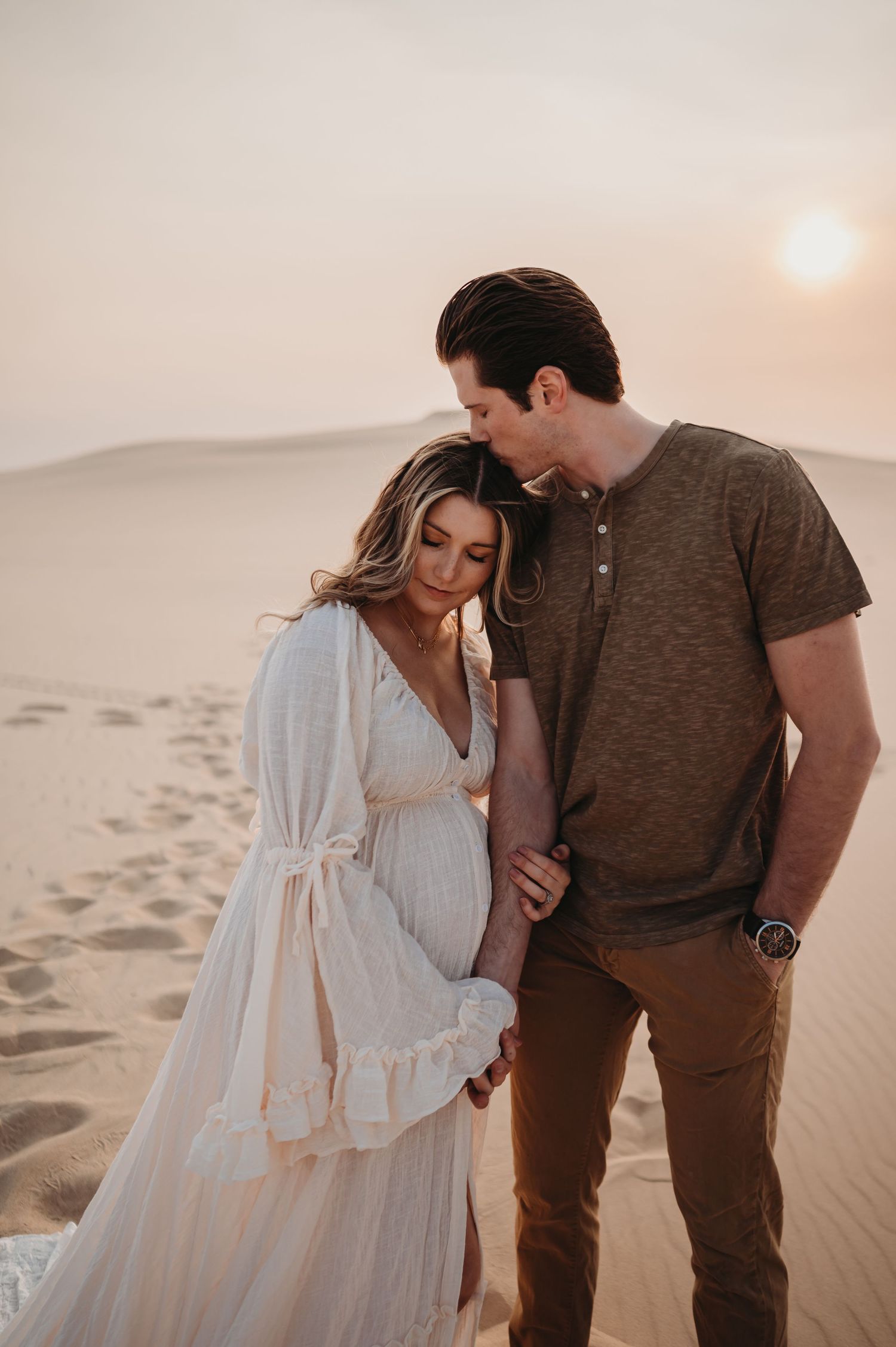 Couple embraces during sunset photoshoot in desert landscape wearing casual and flowing attire.