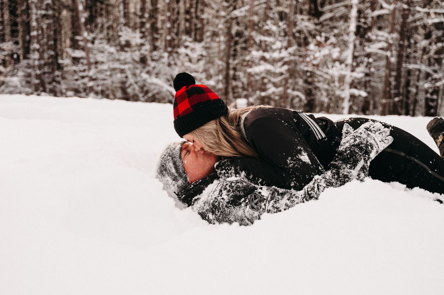 Person wearing buffalo plaid beanie lying in fresh powder snow.