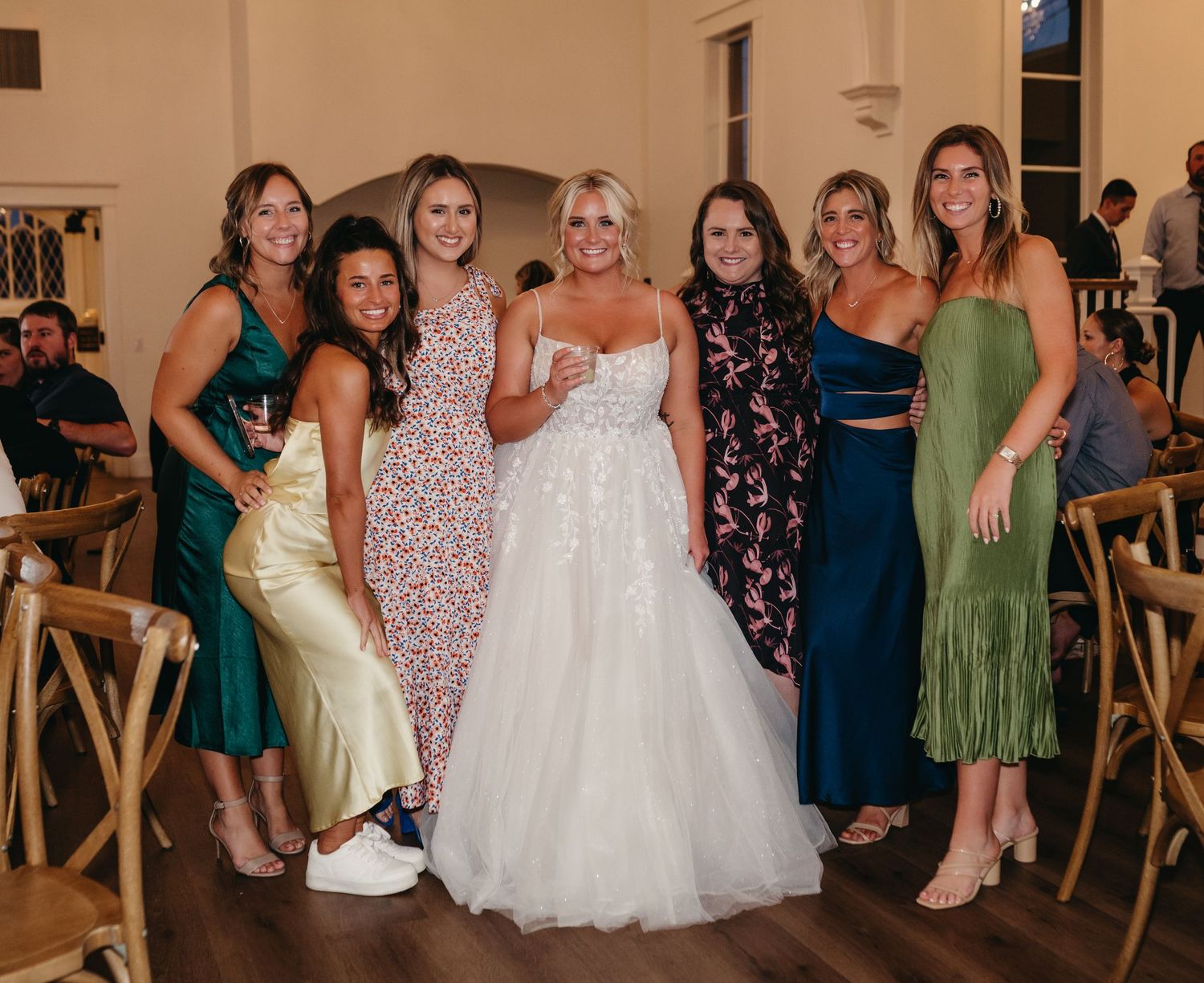 Wedding party poses in colorful dresses at elegant indoor reception venue.
