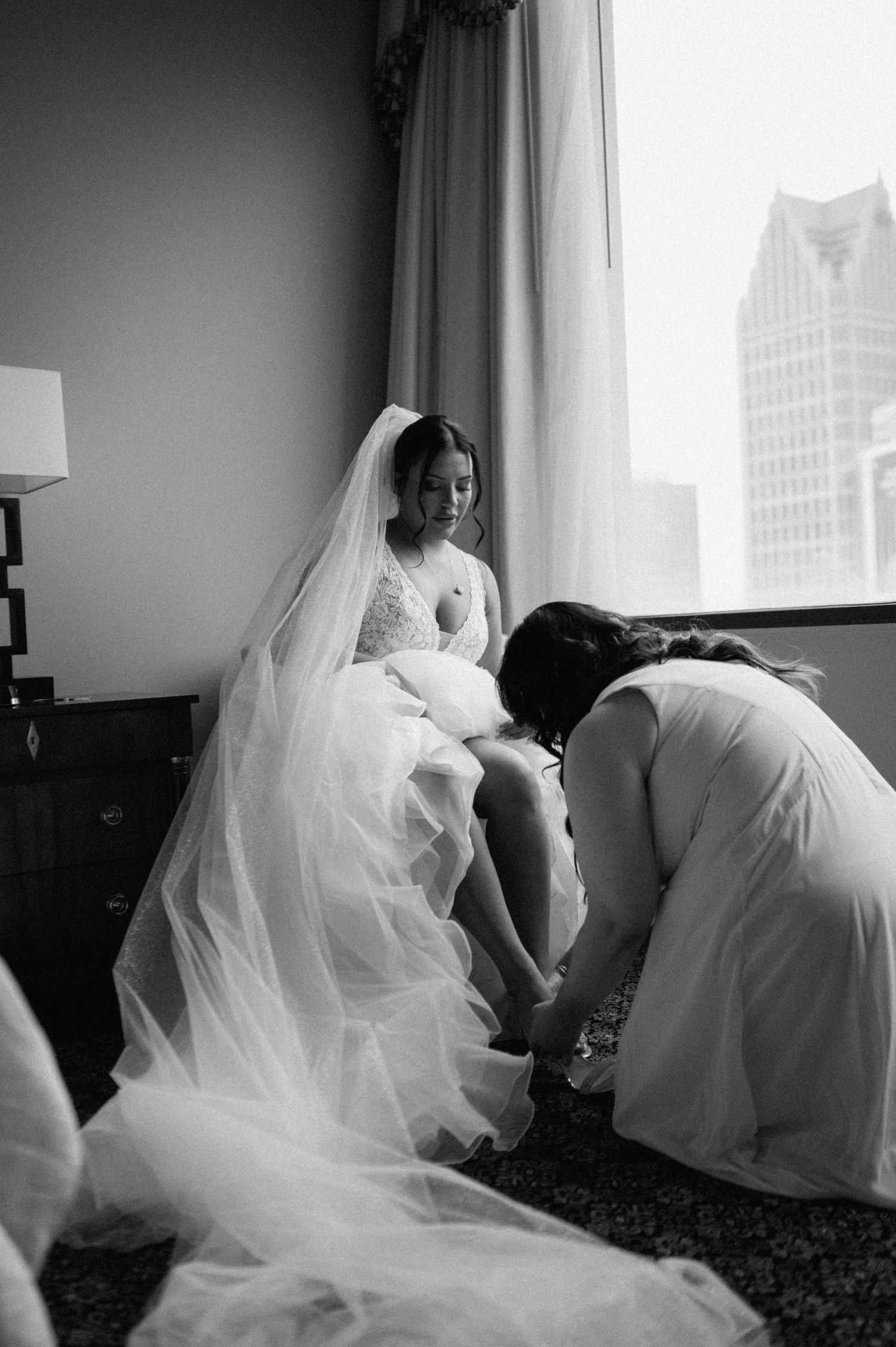 Dramatic black and white photo of a flowing wedding dress and veil against a city backdrop.