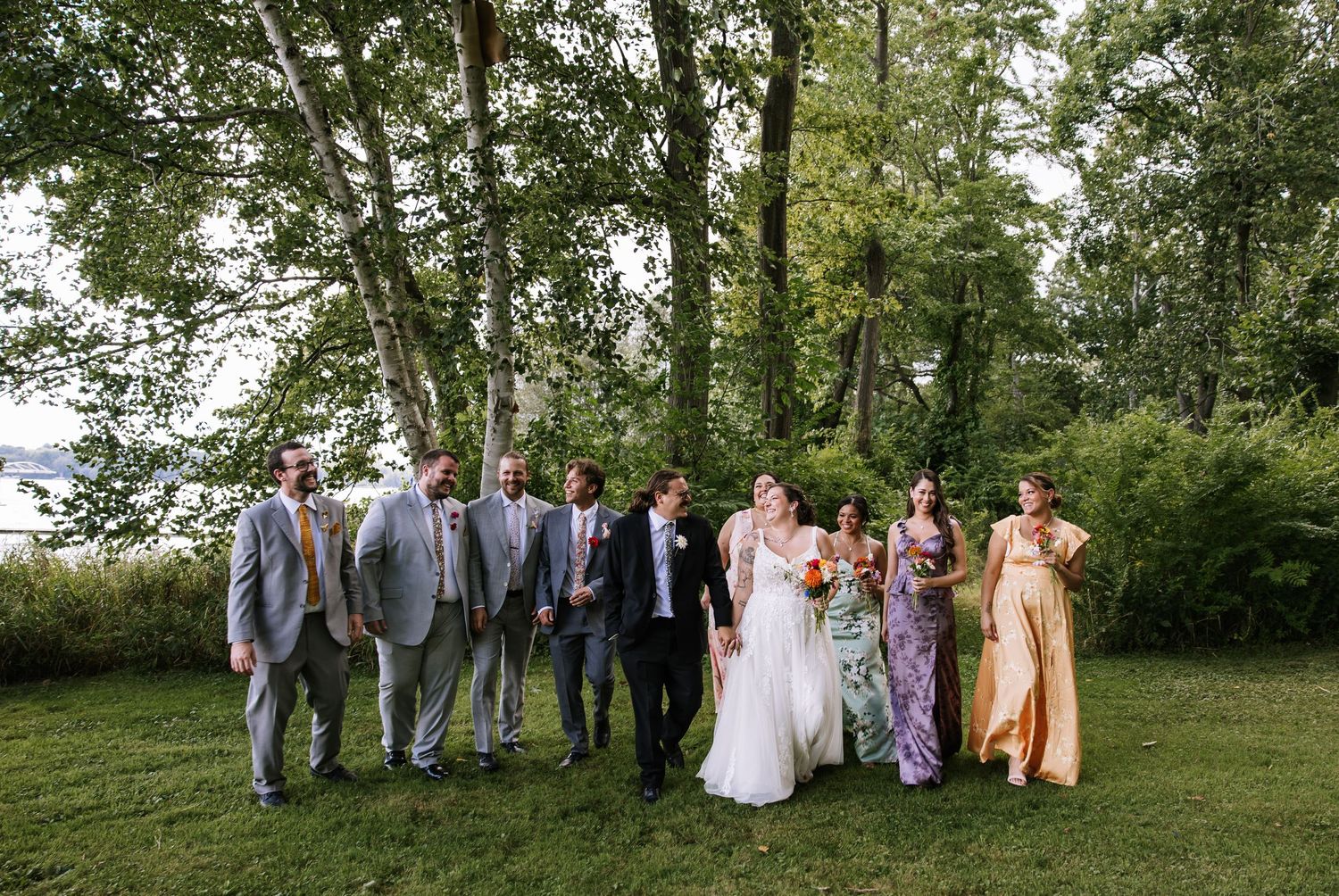 Wedding guests gather for a group photo on a grassy hill surrounded by trees.