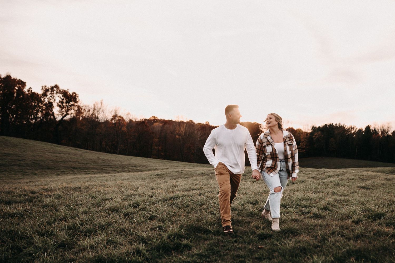 Couple walking hand in hand through sunset meadow.