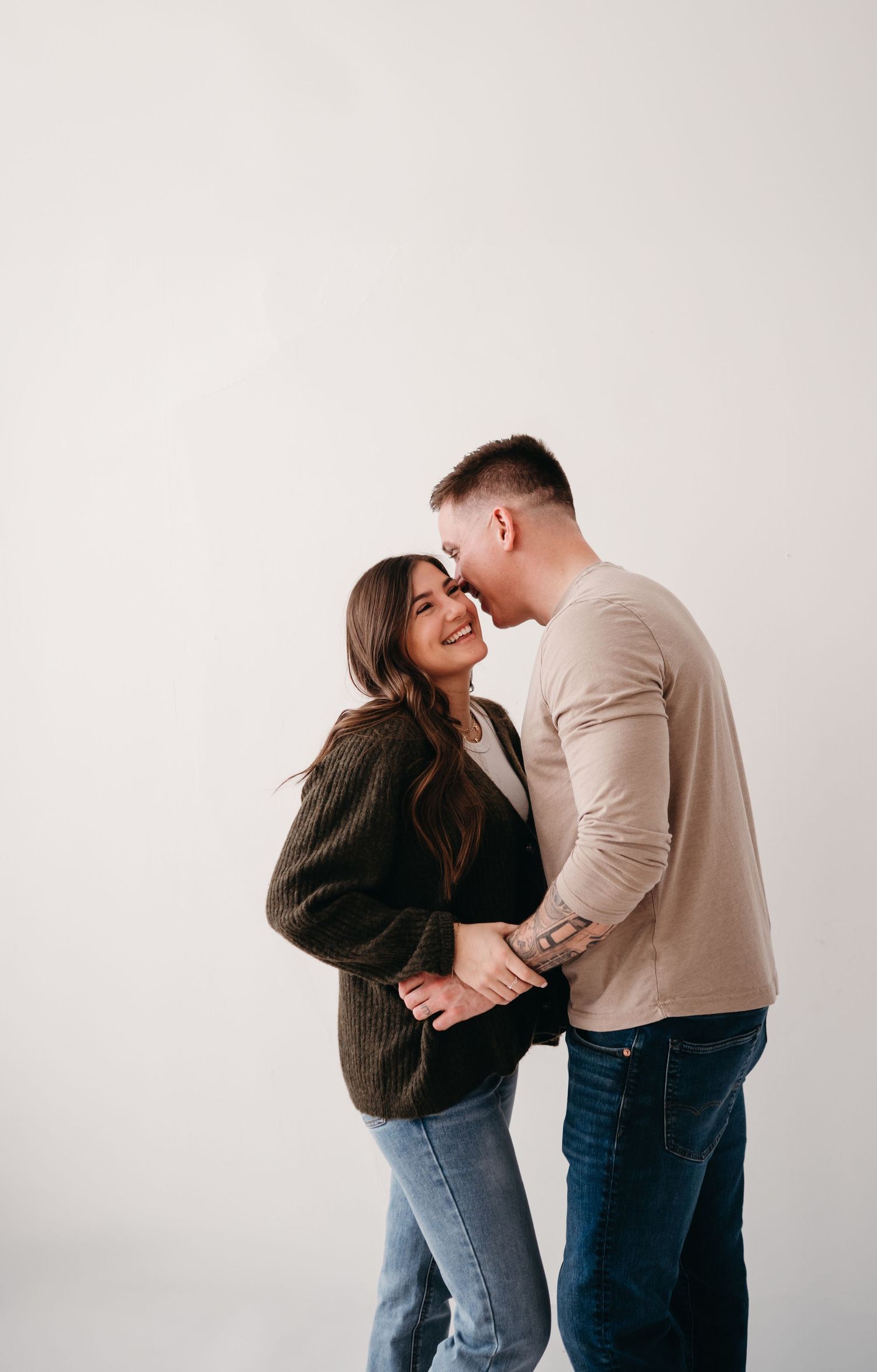 A romantic couple shares an intimate moment while wearing casual outfits against a white background.