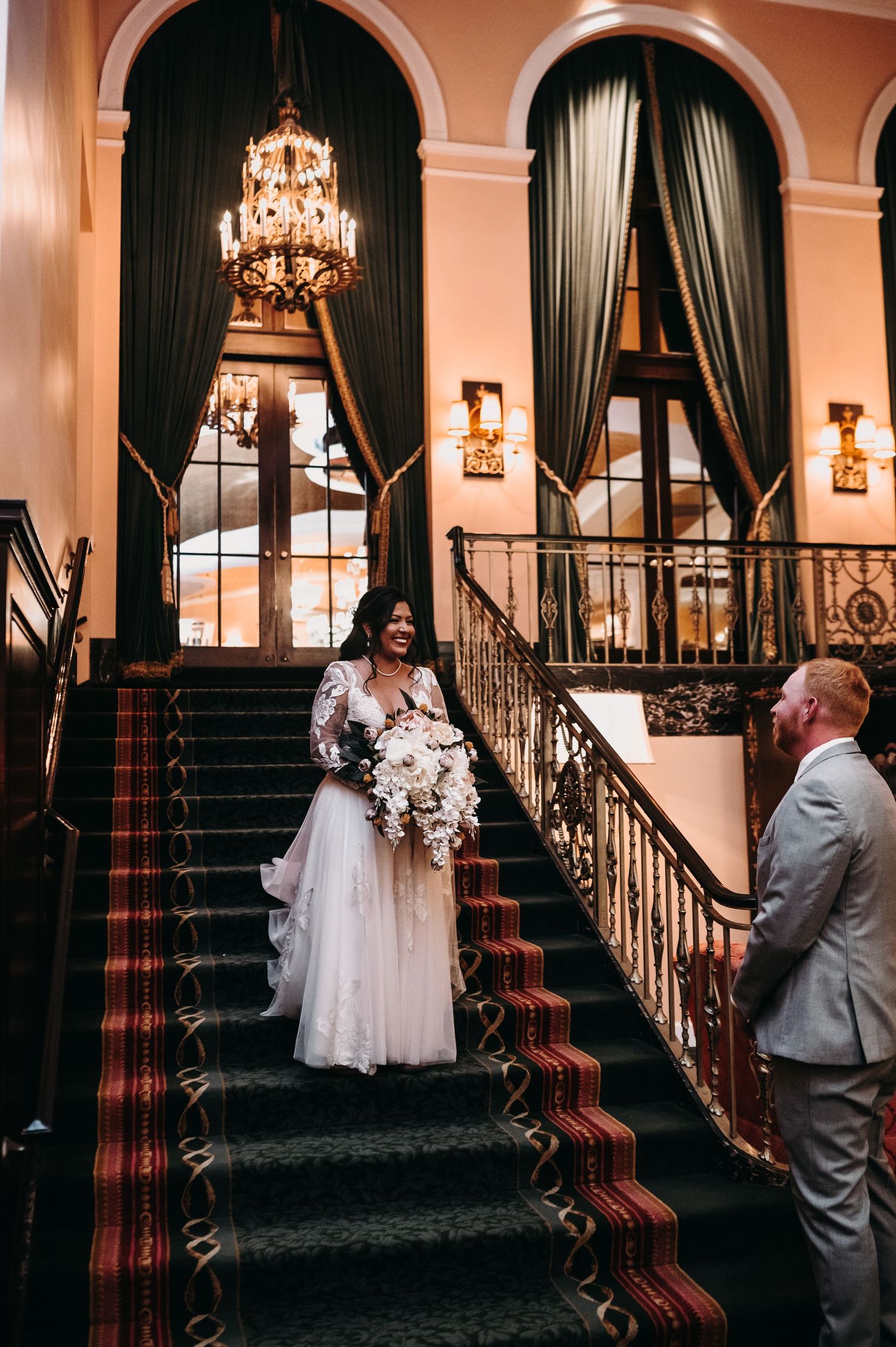 An elegant staircase moment captured during a wedding with ornate chandeliers and arched doorways.