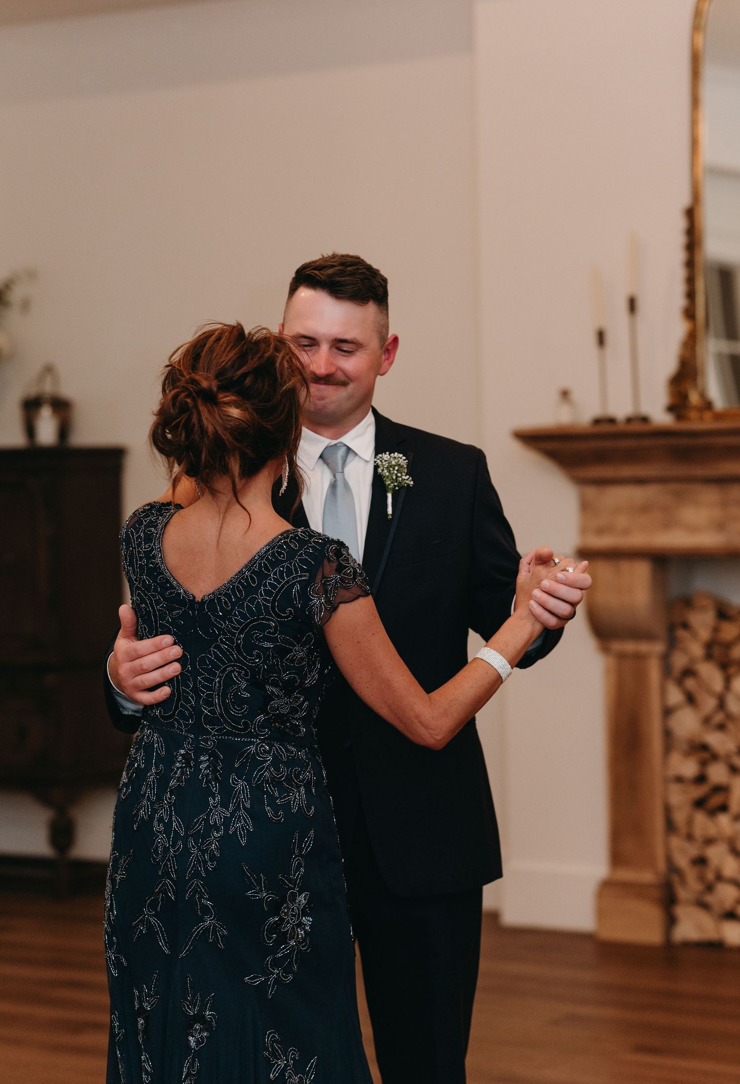 A couple shares an intimate dance at a wedding reception with an elegant fireplace in the background.