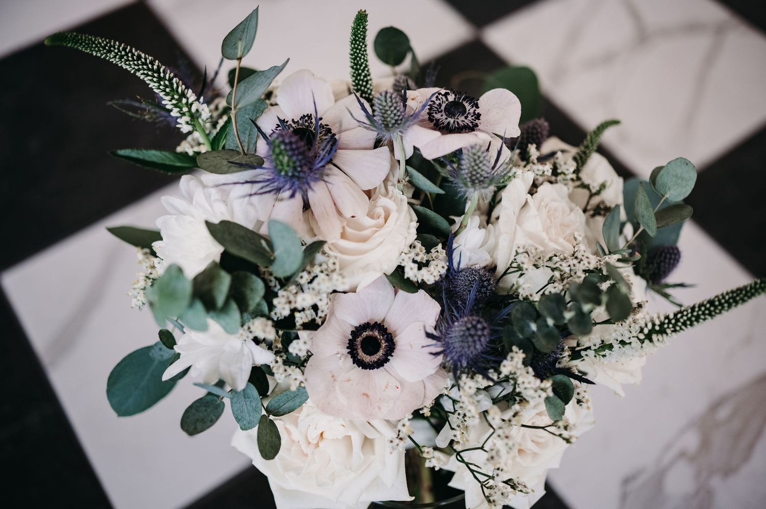 Elegant wedding bouquet featuring white roses, anemones, and eucalyptus on a checkered surface.