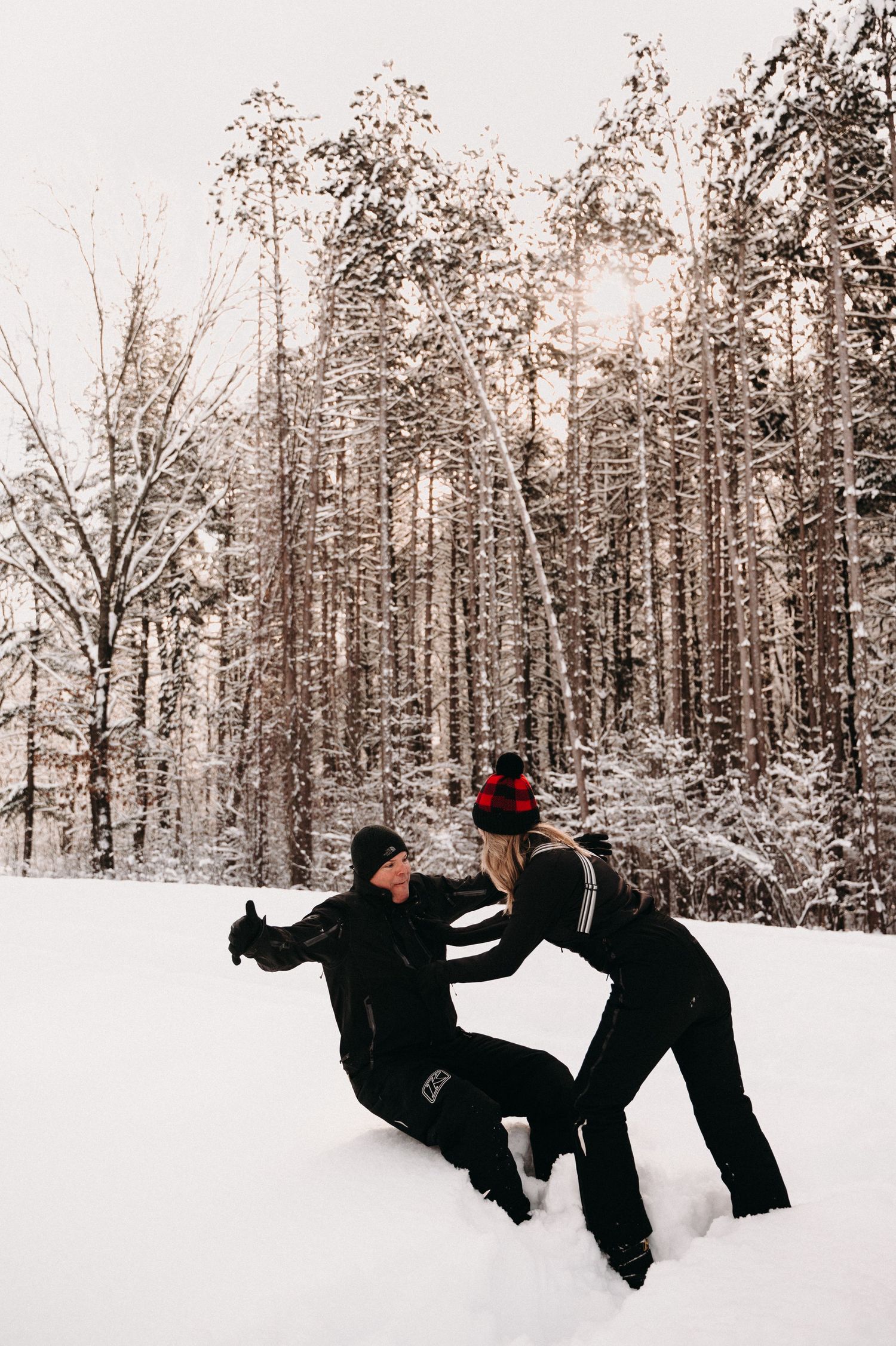 Winter forest scene with couple playing in deep snow among tall trees.