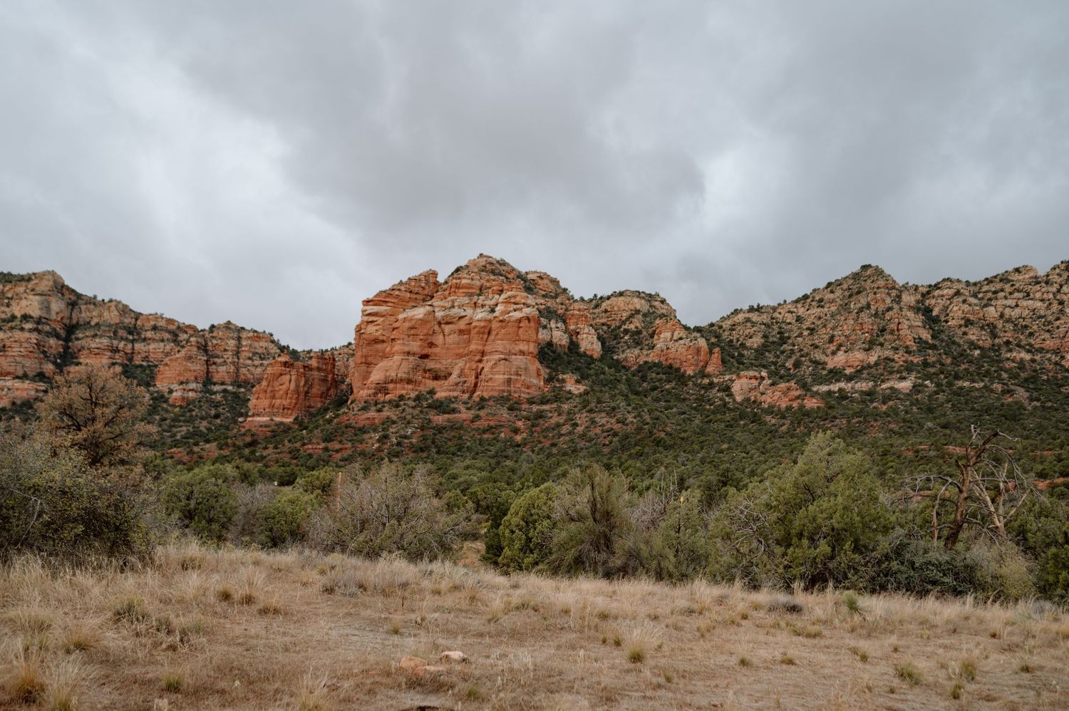Dramatic red rock cliffs and desert landscape under overcast sky.