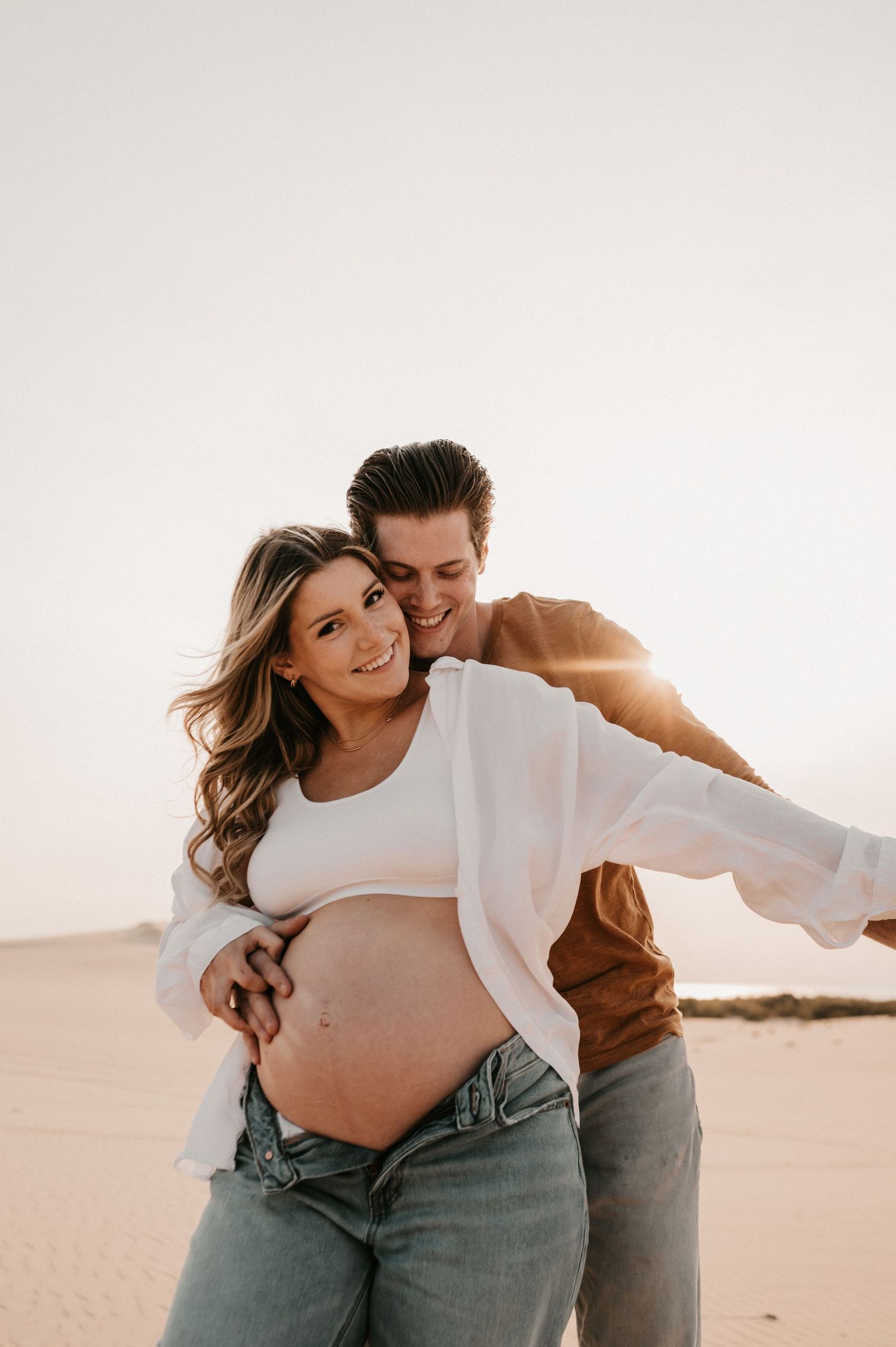 Intimate desert maternity photo with couple sharing tender moment against sand dunes.