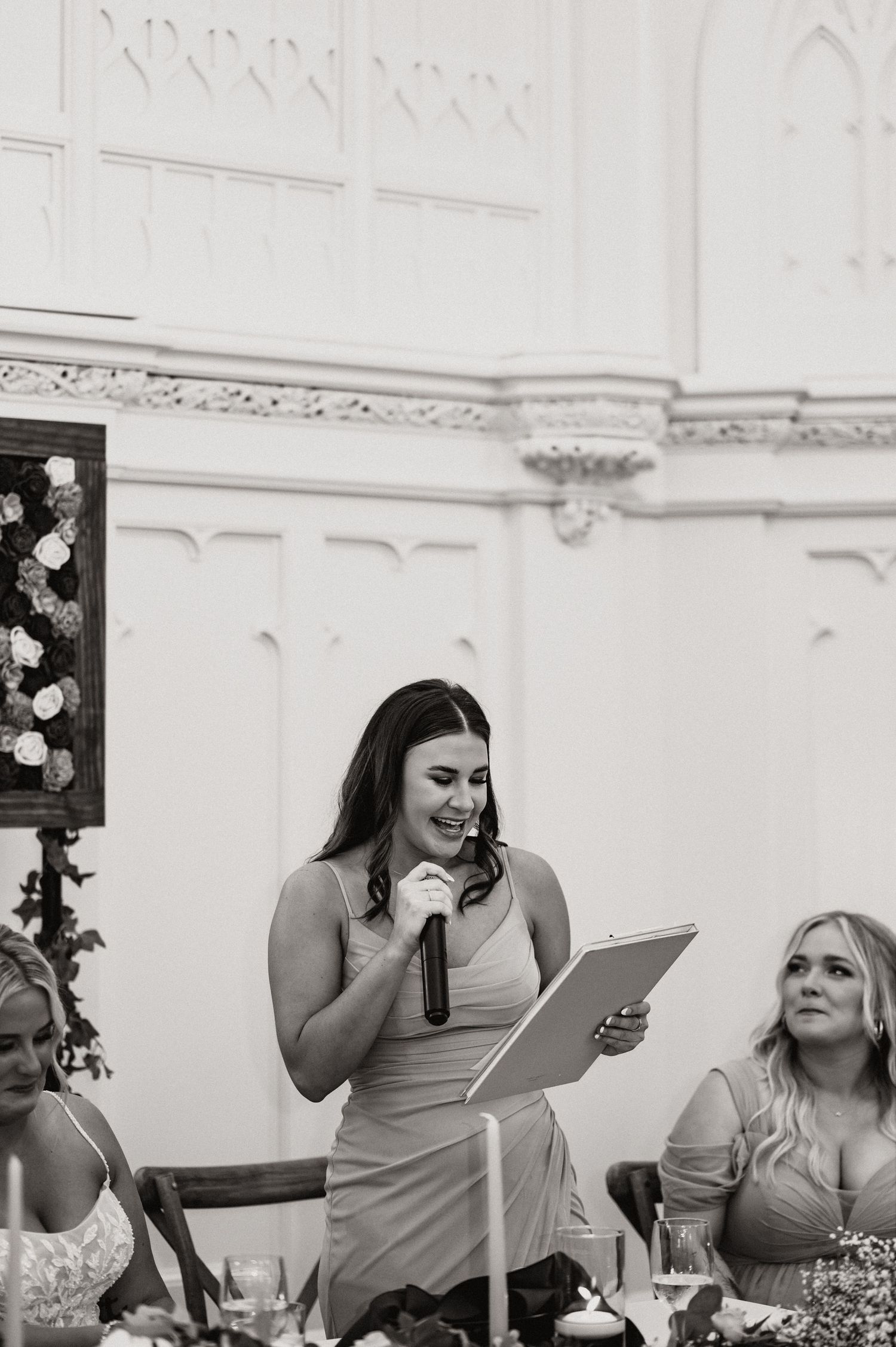 Wedding reception speech being given in an ornate white-walled venue with decorative molding.