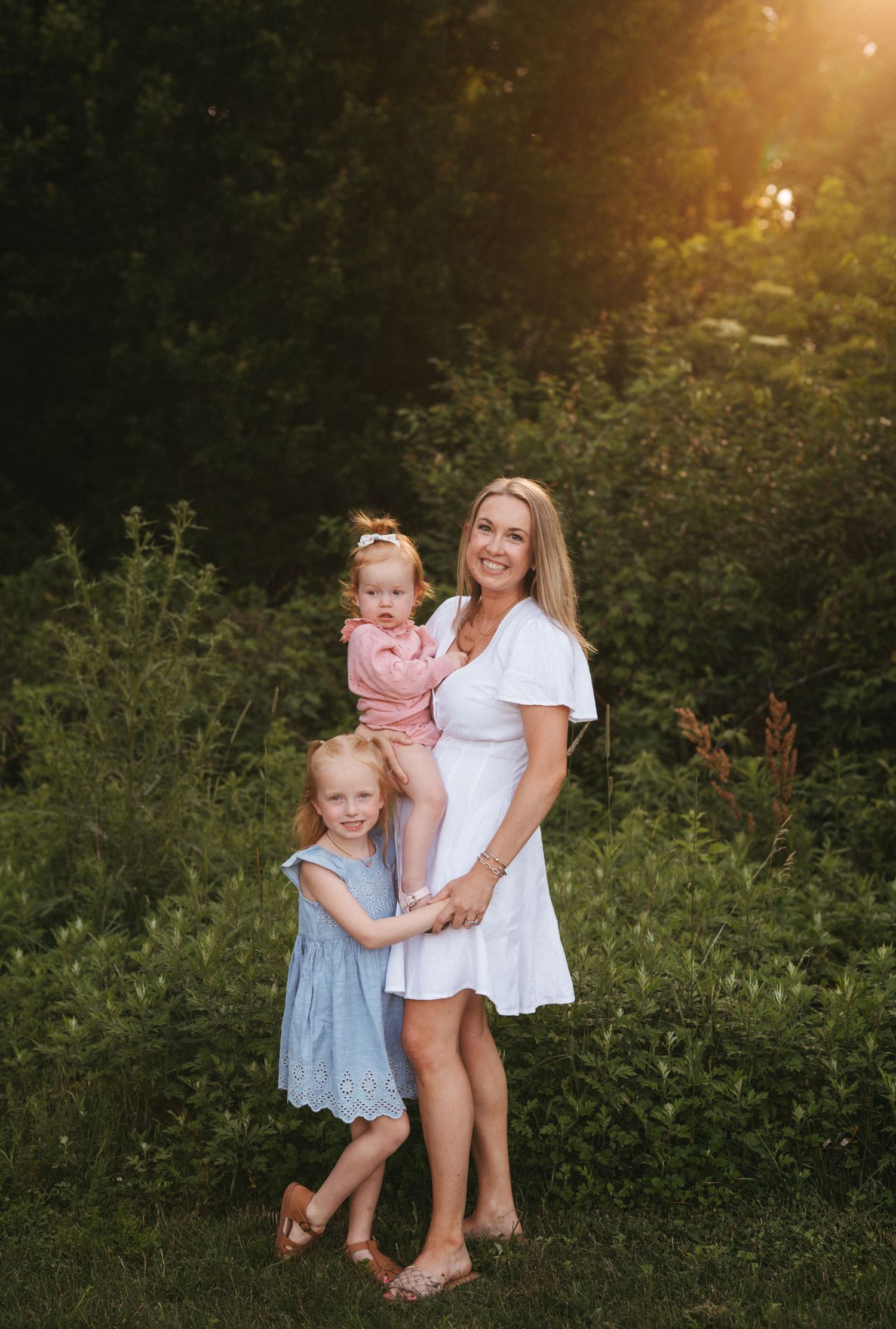 Family group sharing playful moment together in garden with golden sunset lighting.