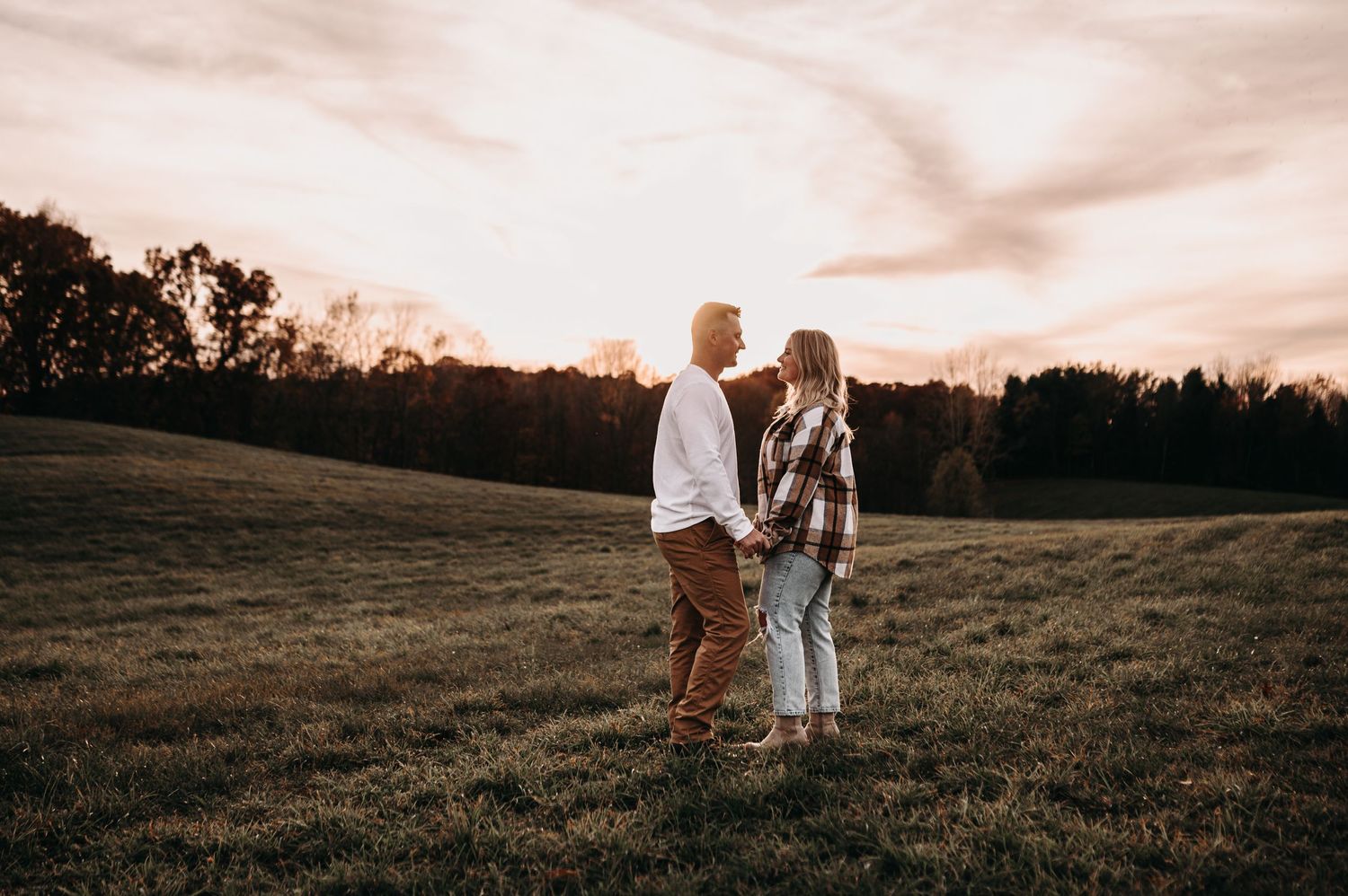 Couple sharing intimate moment in rustic field at dusk.