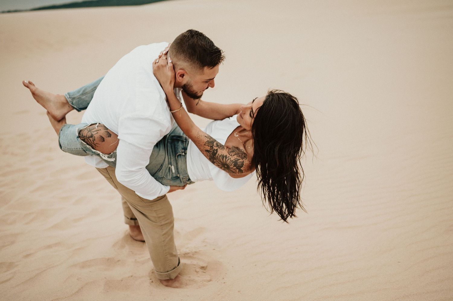 A playful dip pose captured on sandy dunes during a couples photoshoot.