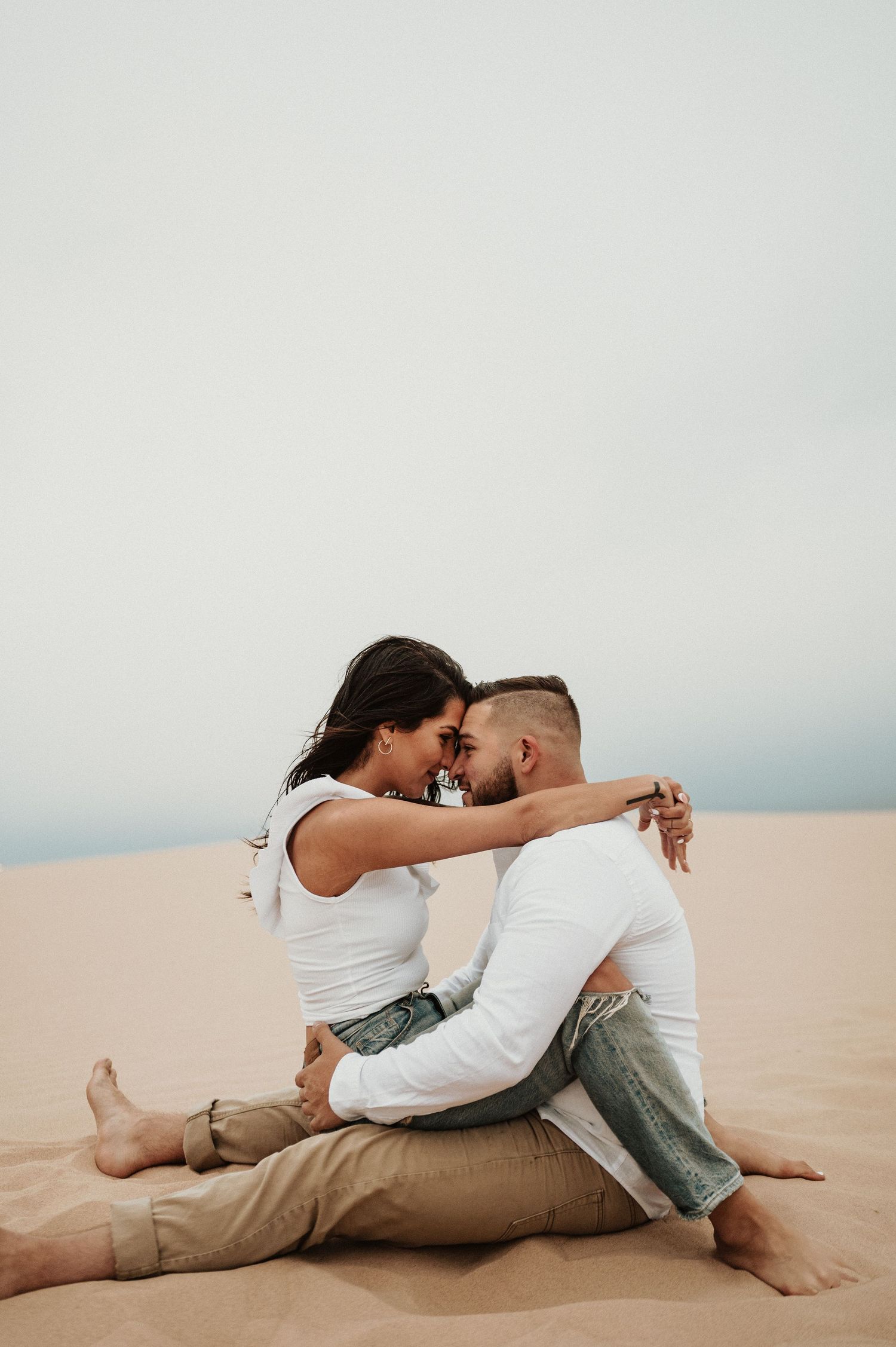A couple shares an intimate moment while sitting on desert sand dunes.