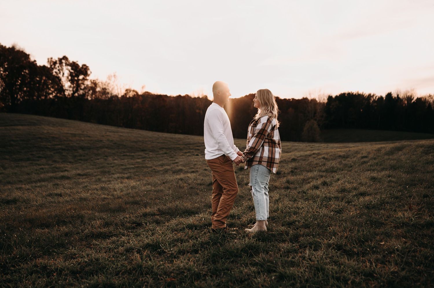 Couple standing together in autumn field during golden hour.