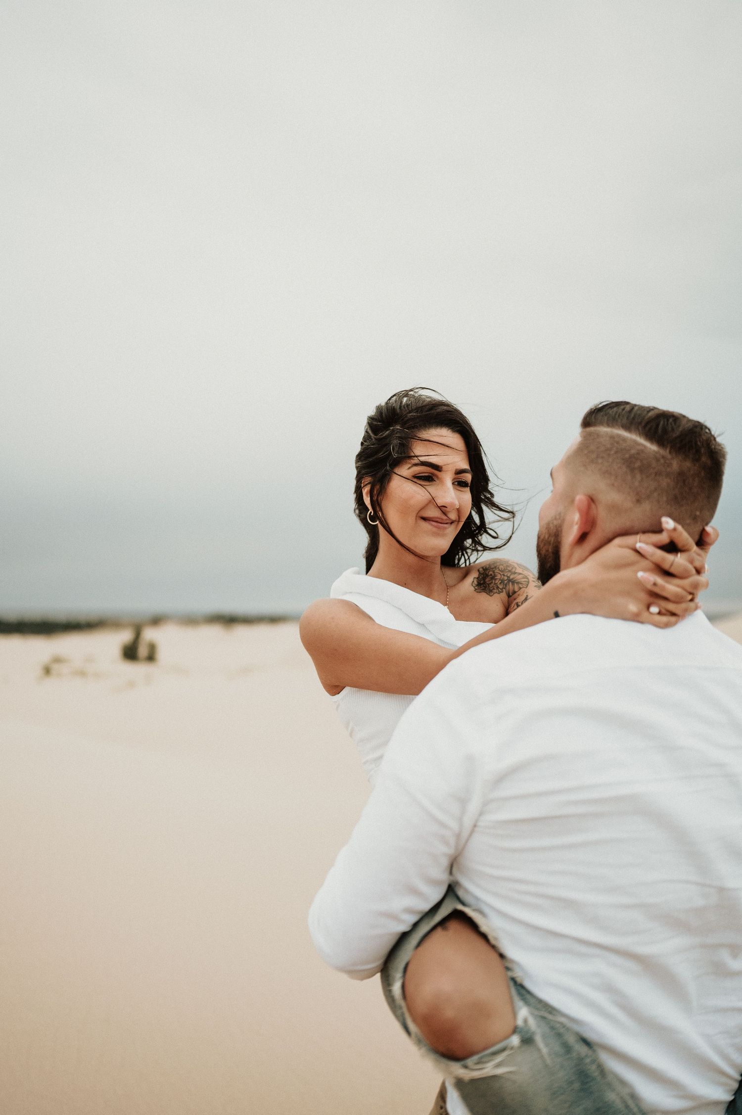 A couple embraces on sand dunes during a romantic desert photoshoot.