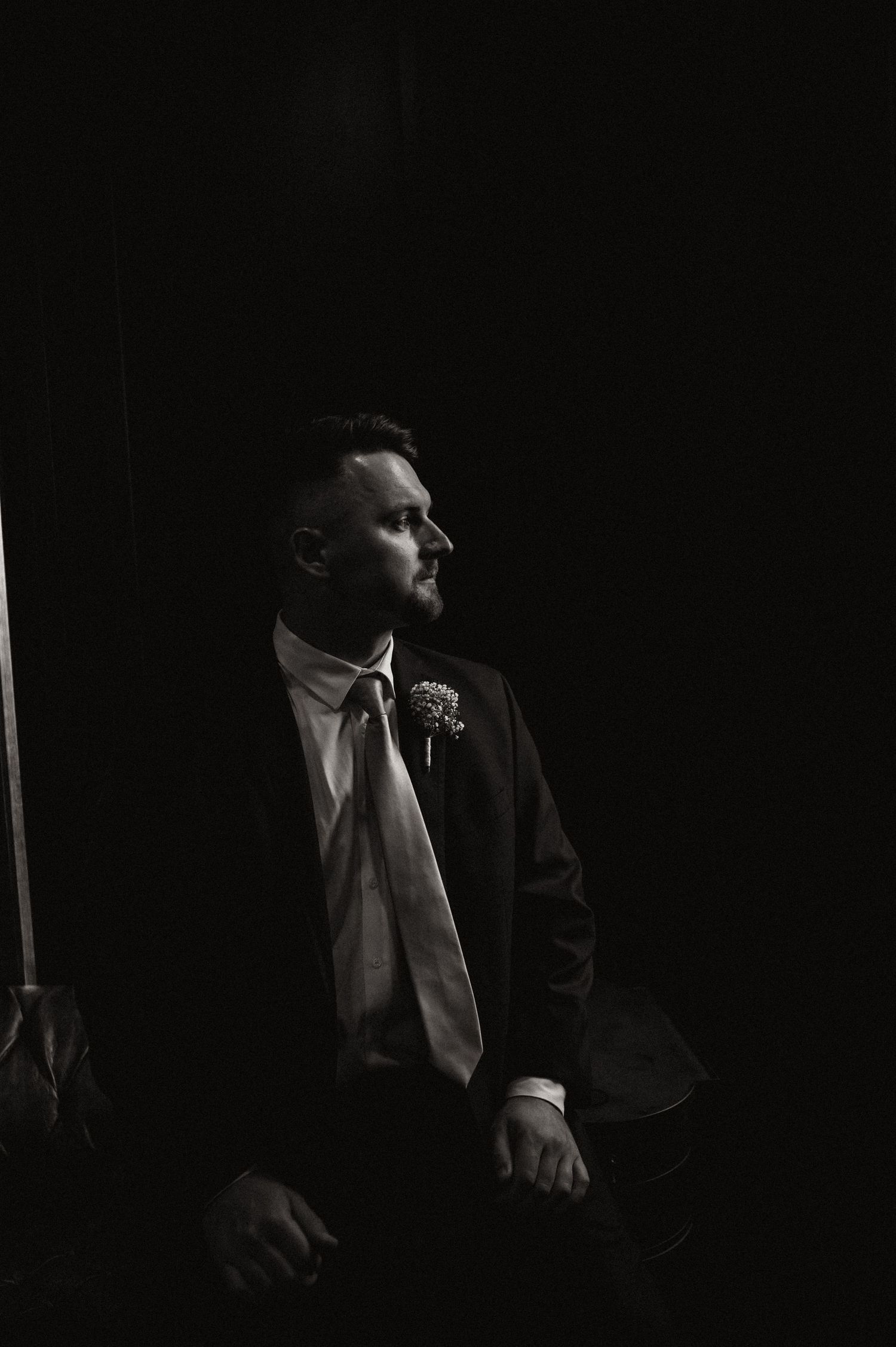 Moody black and white portrait of a person in formal attire with boutonniere.