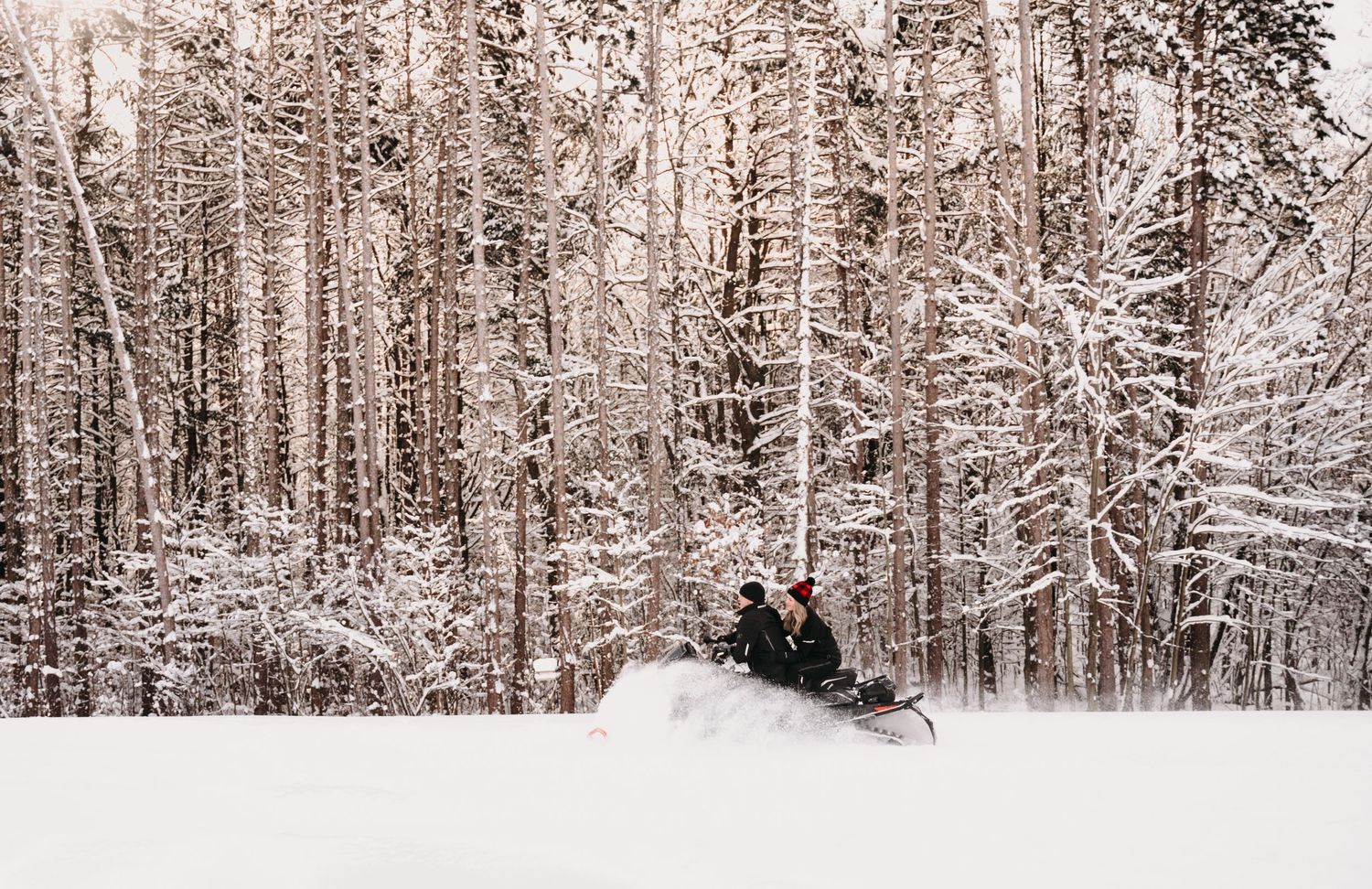 Snowmobilers taking a break in a serene winter forest landscape.