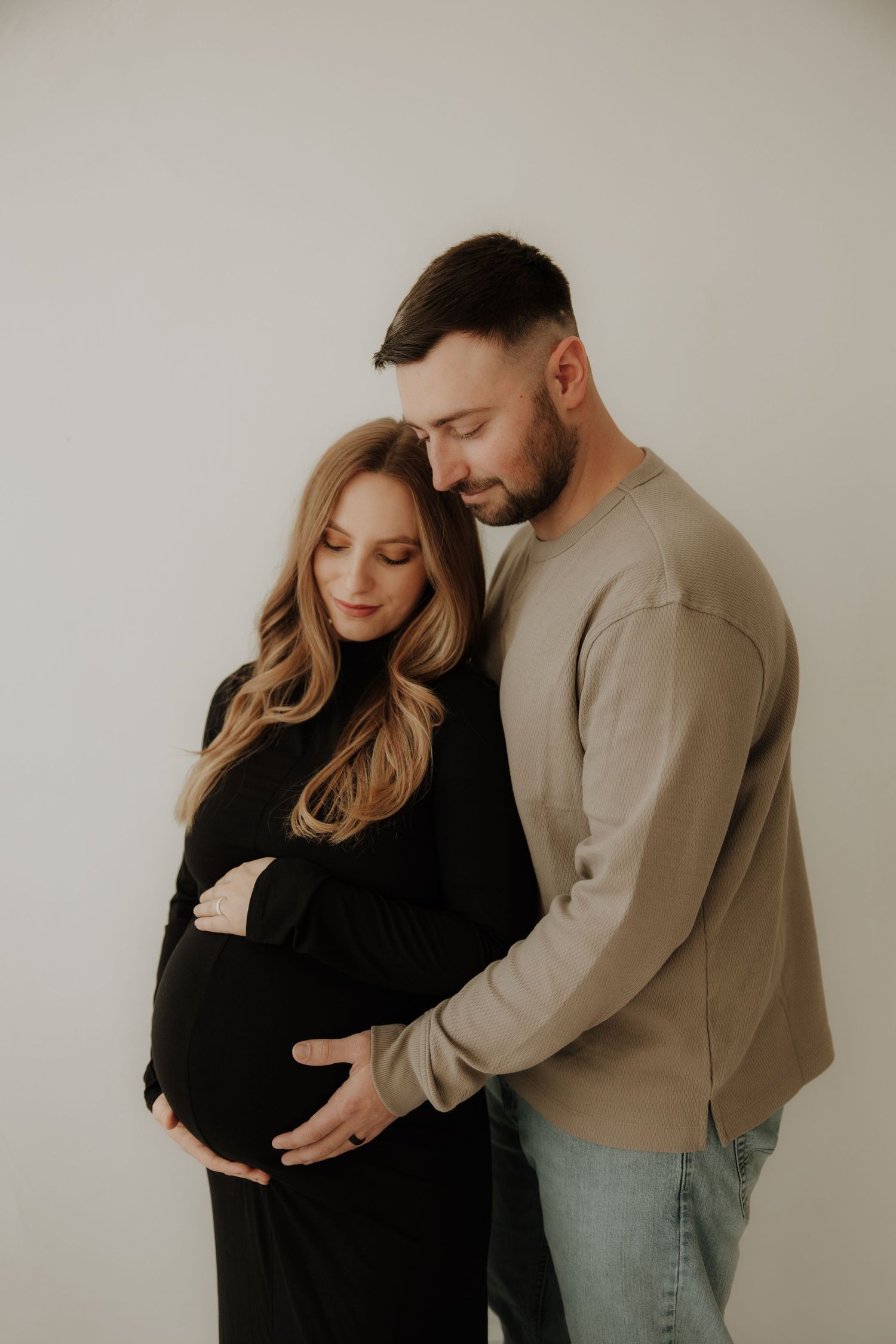 Couple sharing tender moment during maternity photoshoot in casual attire.