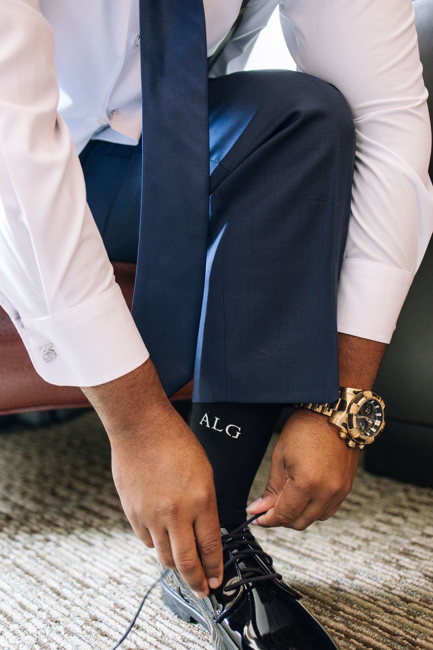 Close-up of groom putting on black formal shoes with monogrammed socks.