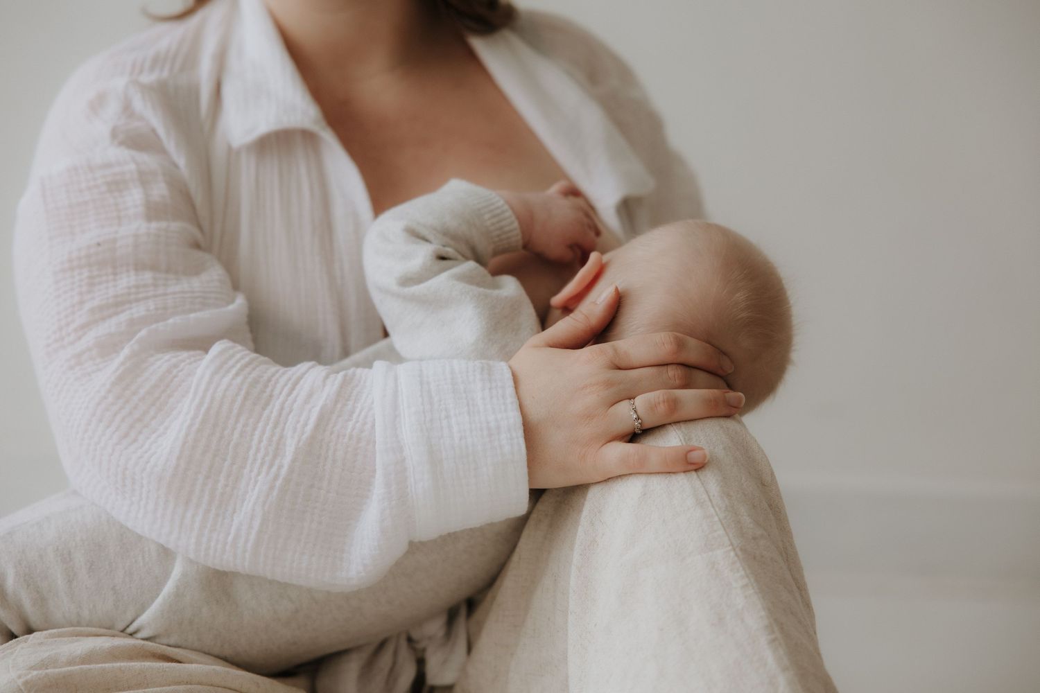 Close-up of mother in white muslin shirt breastfeeding infant, wearing ring.