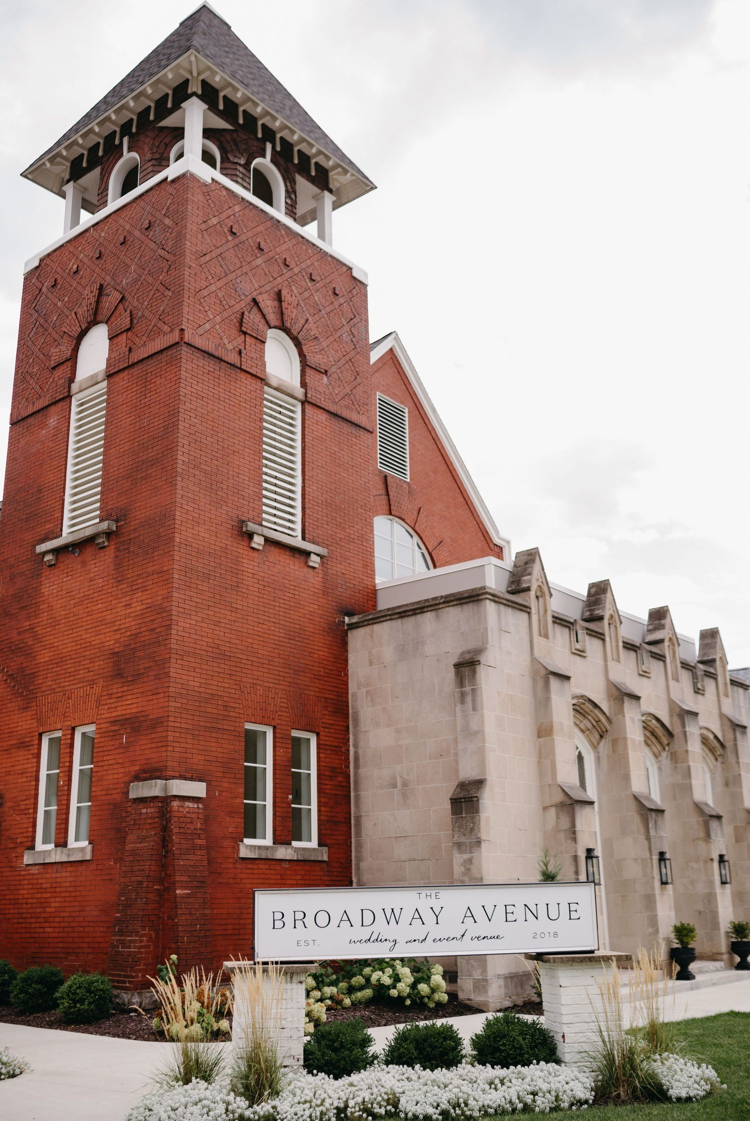 Exterior view of Broadway Avenue church with red brick tower and white stone architectural details.