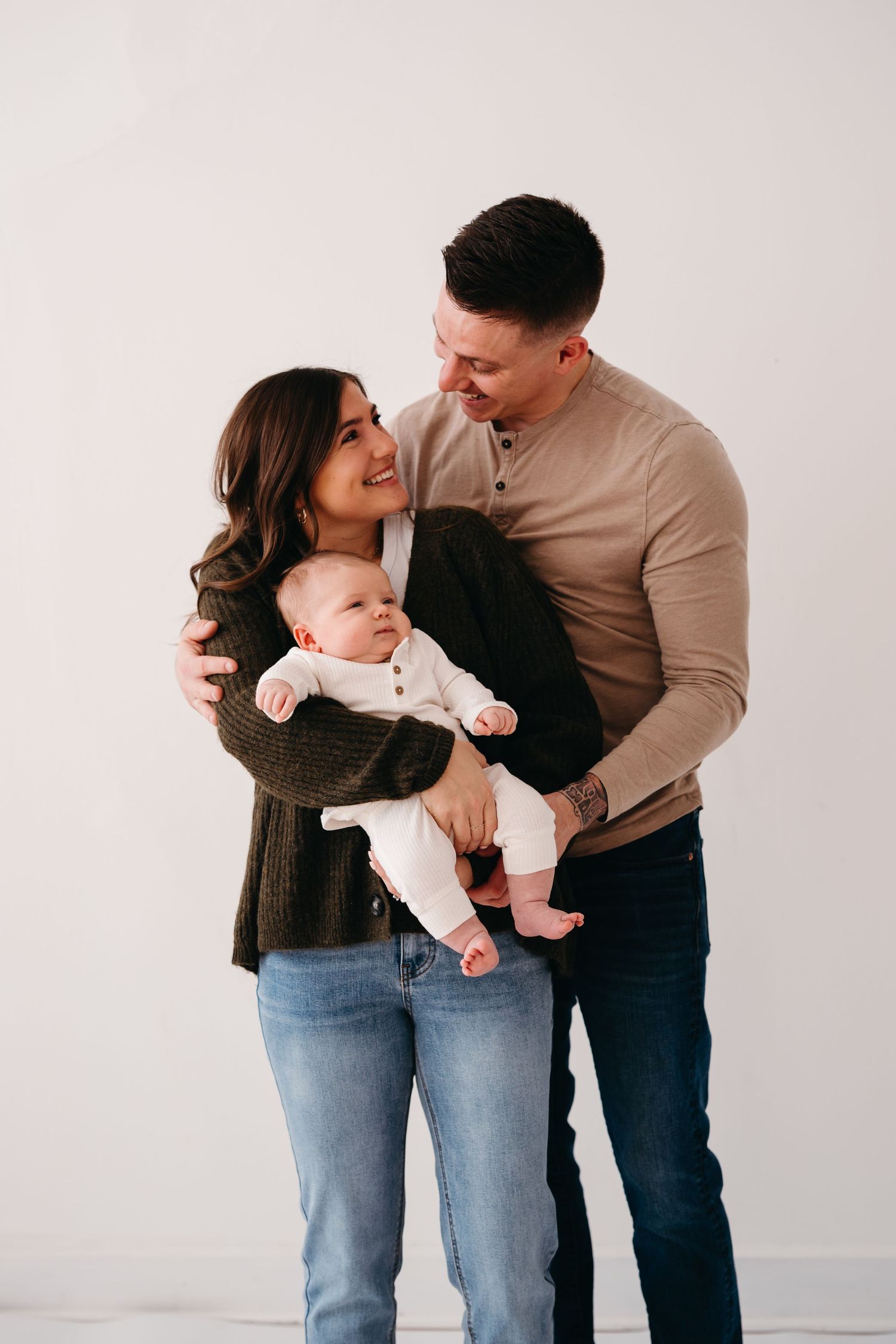 A young family poses together against a white backdrop while holding their baby in a candid moment.