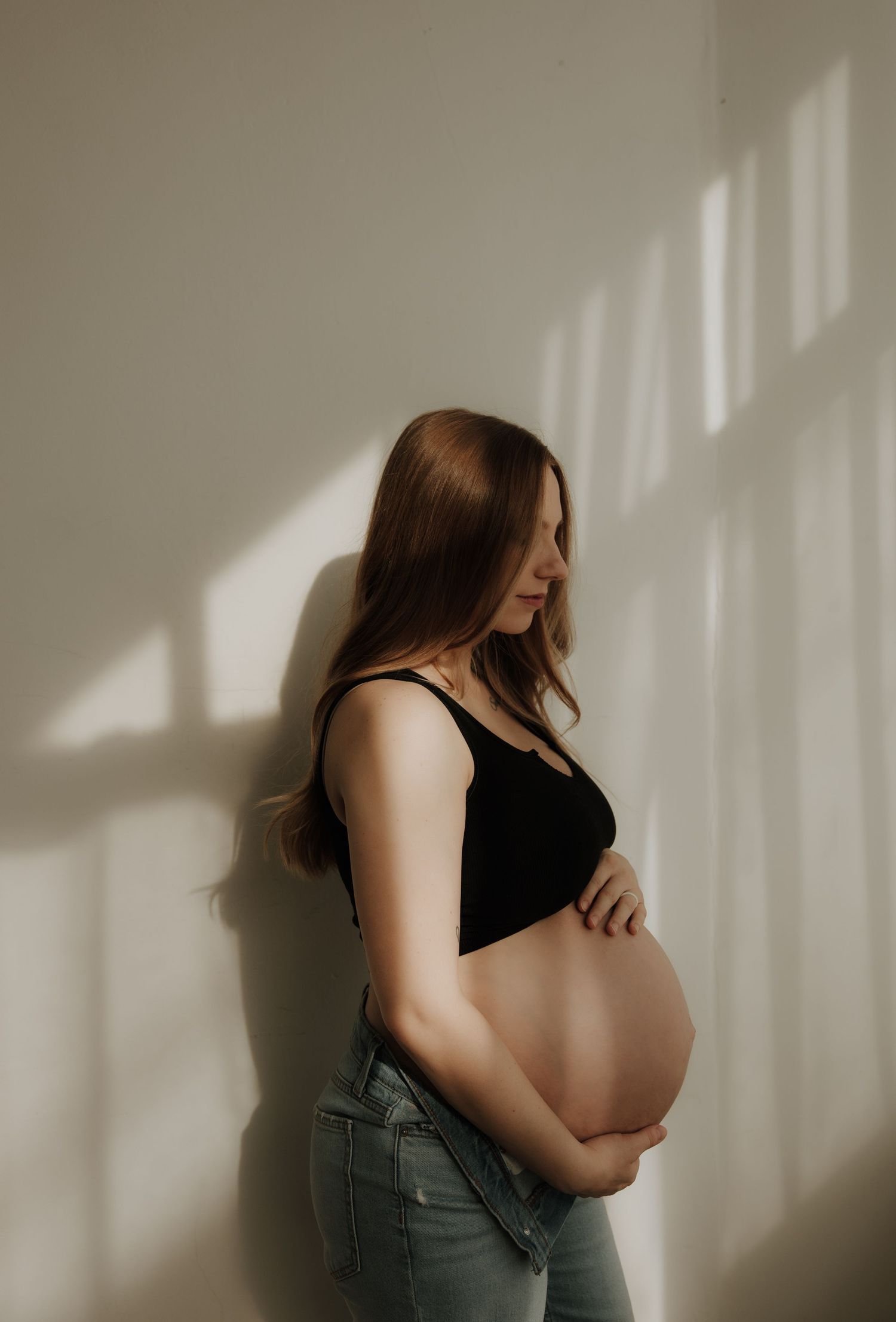 Artistic maternity photos with dramatic window lighting casting shadows on wall.