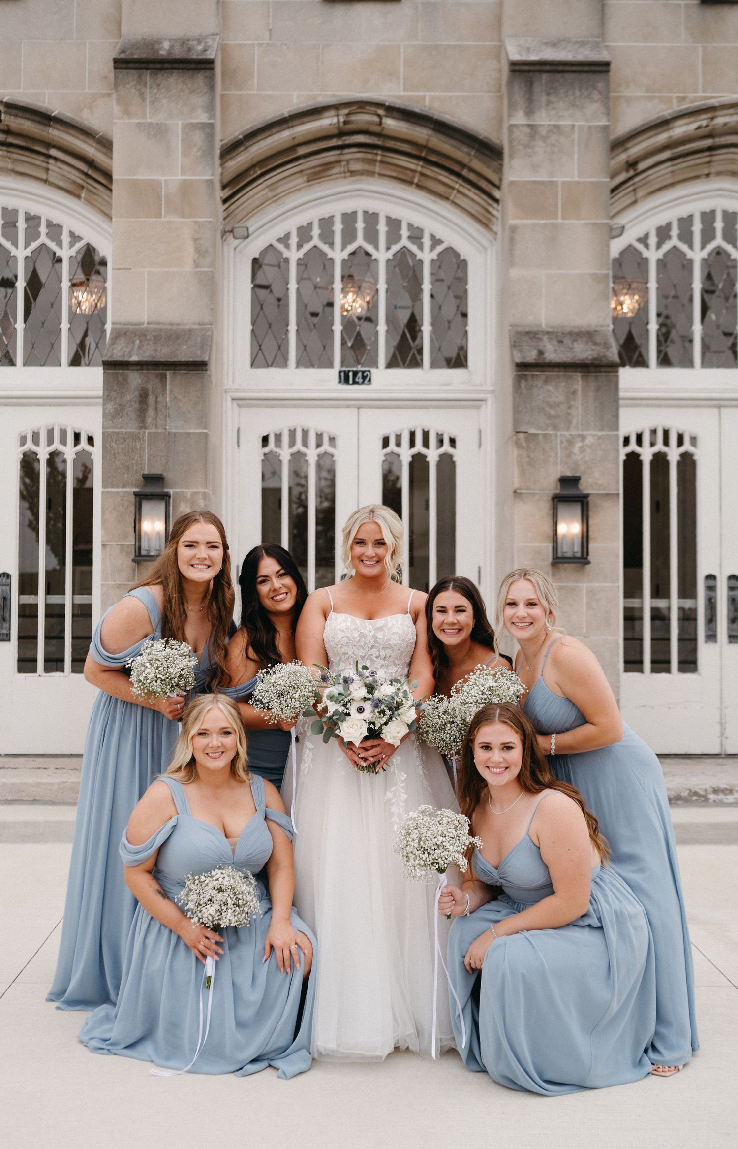 Wedding party in powder blue dresses poses formally against stone church architecture.