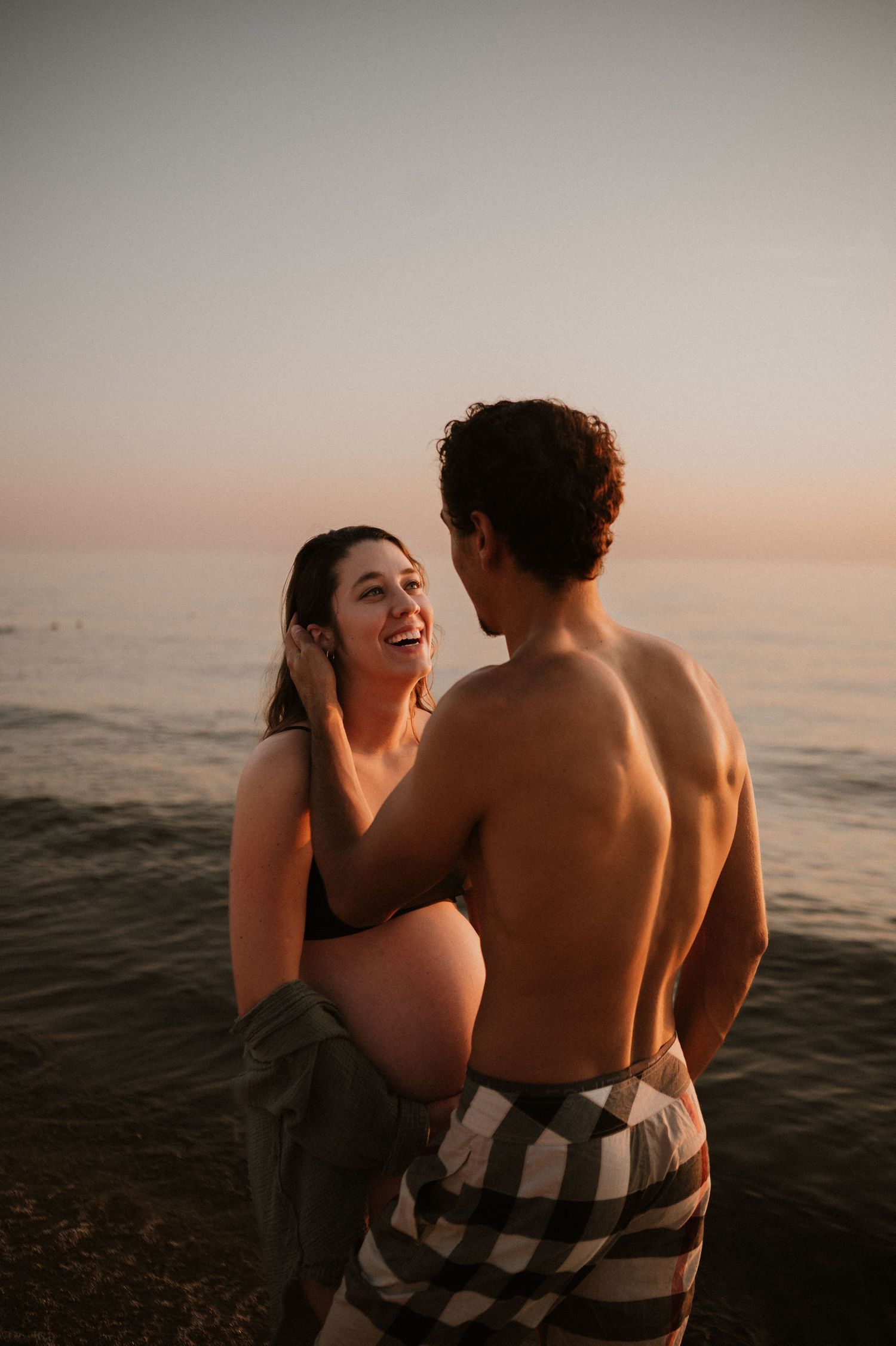 Romantic beach photoshoot with couple laughing together by the water at dusk.