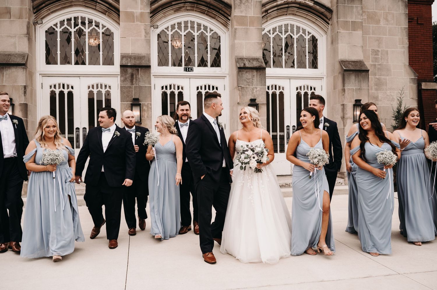 Wedding party in light blue and black attire poses together against gothic church backdrop.