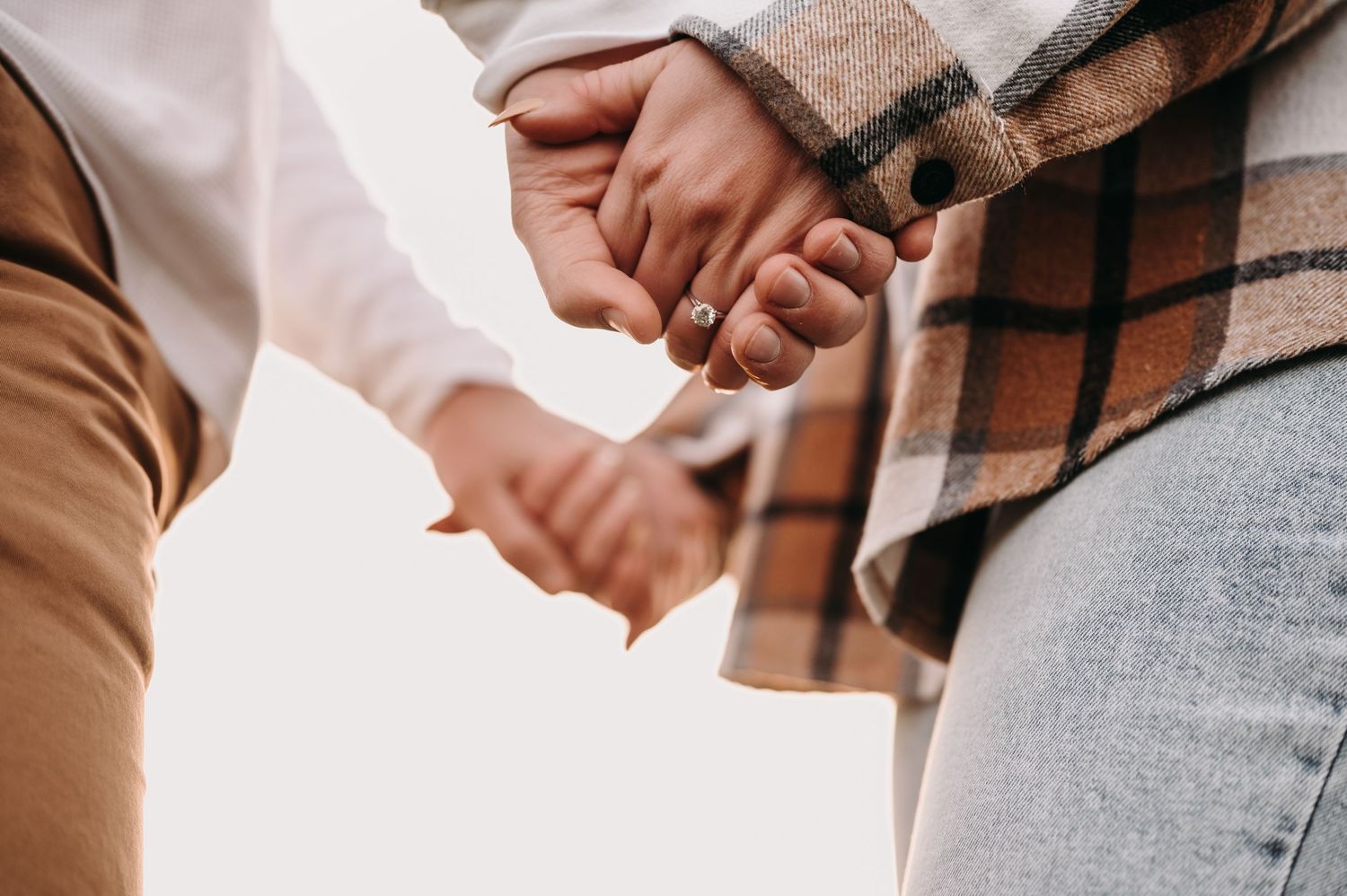 Close up of couple holding hands wearing autumn clothing.